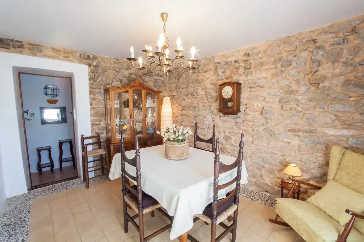 A dining area with a table and chairs sits against exposed stone walls.