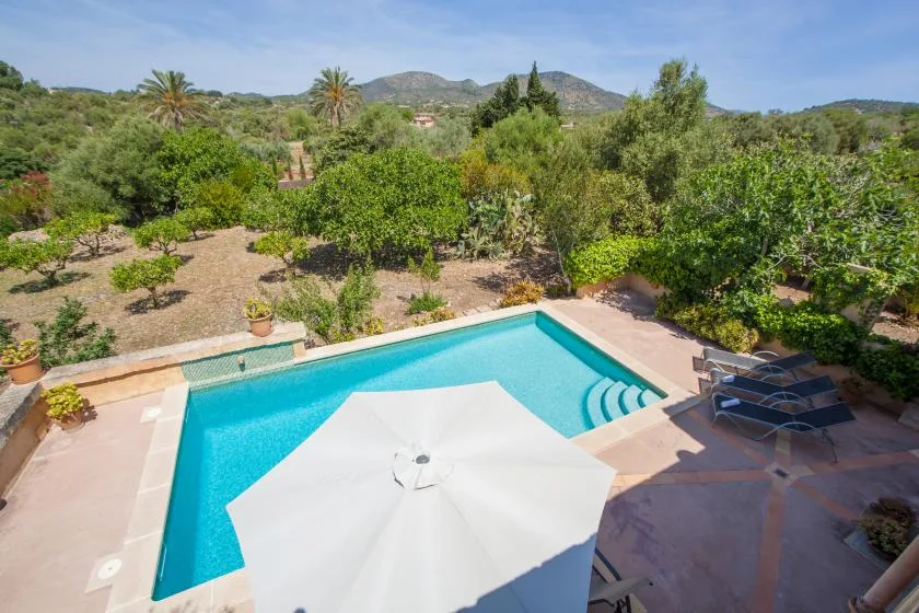 A swimming pool with a white umbrella, surrounded by trees and hills.