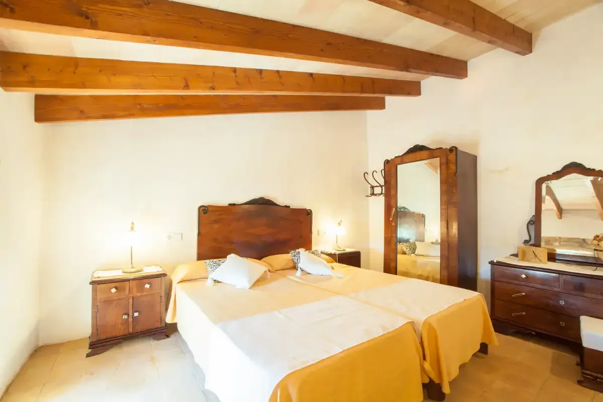 A bedroom with a double bed, wooden ceiling beams, and bedside furniture.