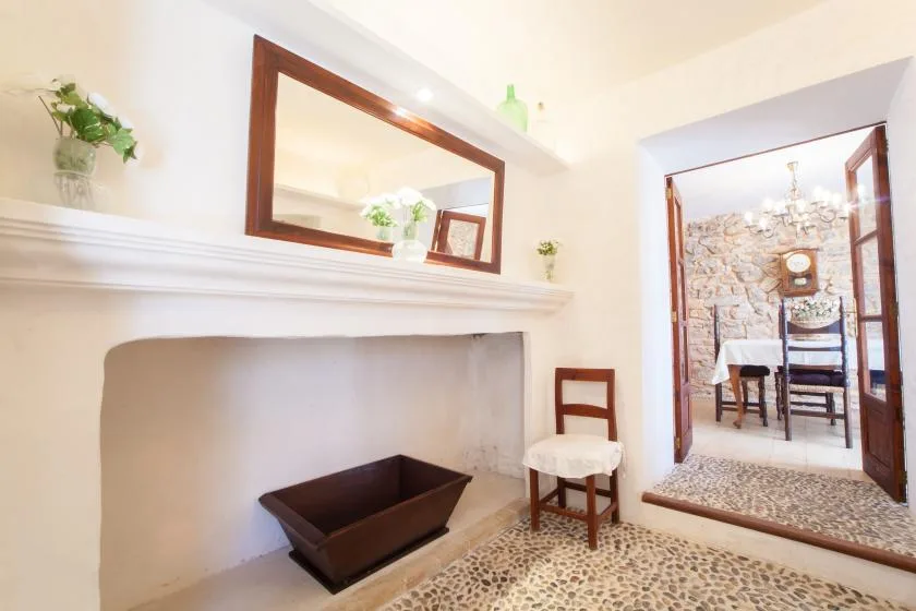 A bright interior with a wide fireplace, a chair, and a doorway into a dining area.