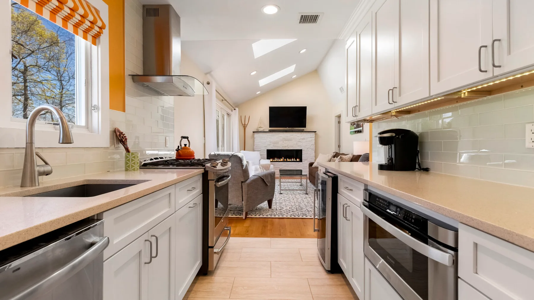 Una cocina luminosa da a una sala de estar con televisor y chimenea.