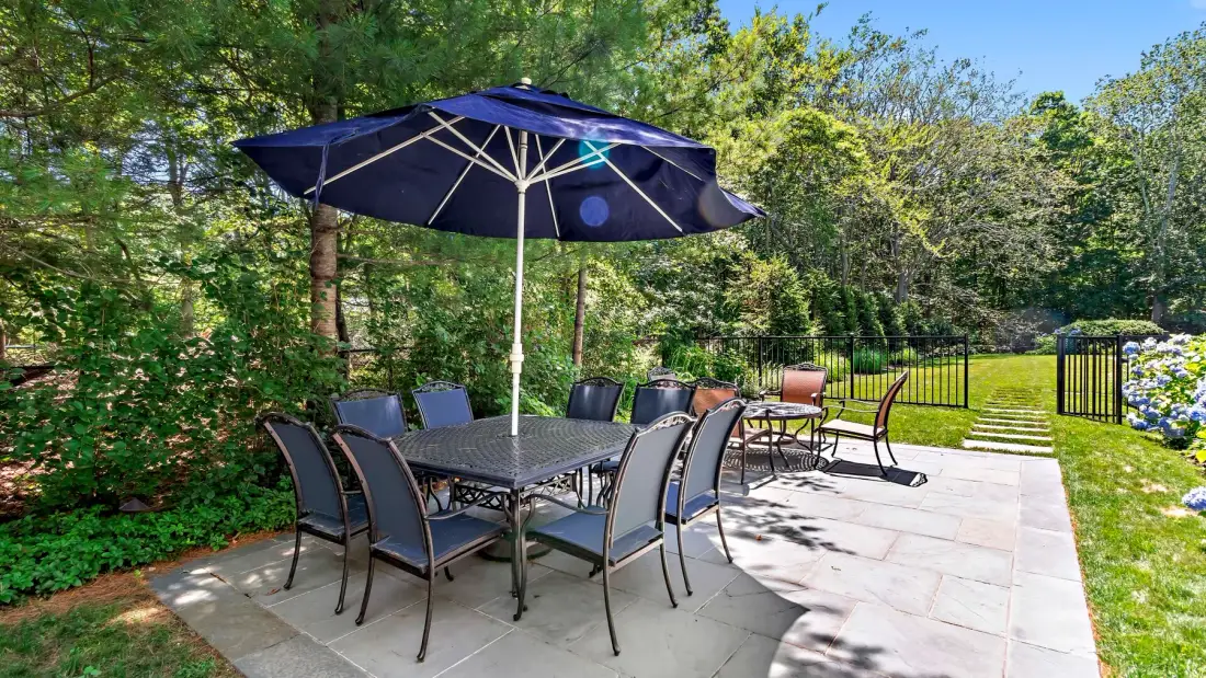 An outdoor patio has a dining table and seating beneath a large umbrella.