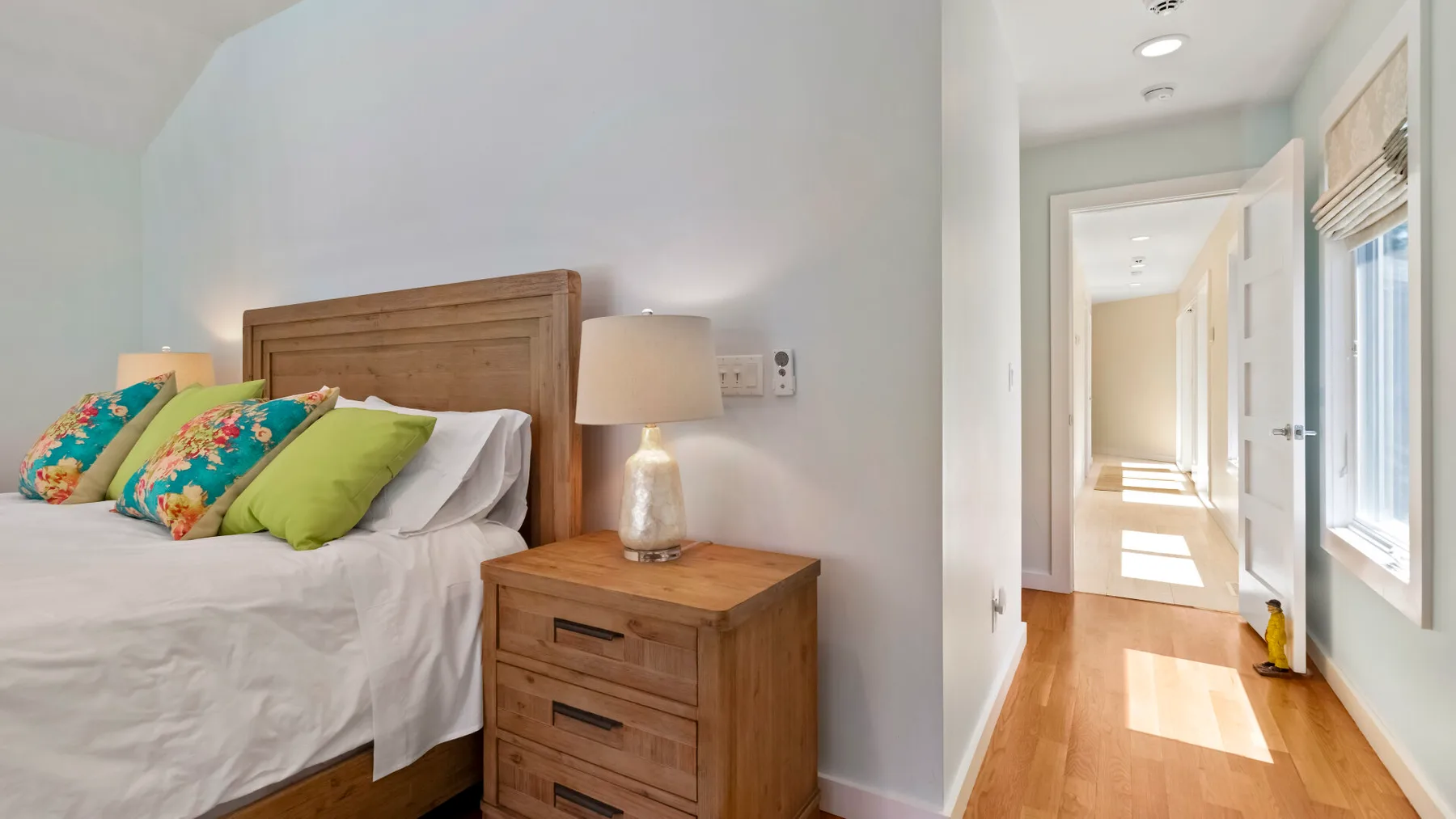 Un dormitorio con una cama junto a una mesita de madera y una puerta abierta.