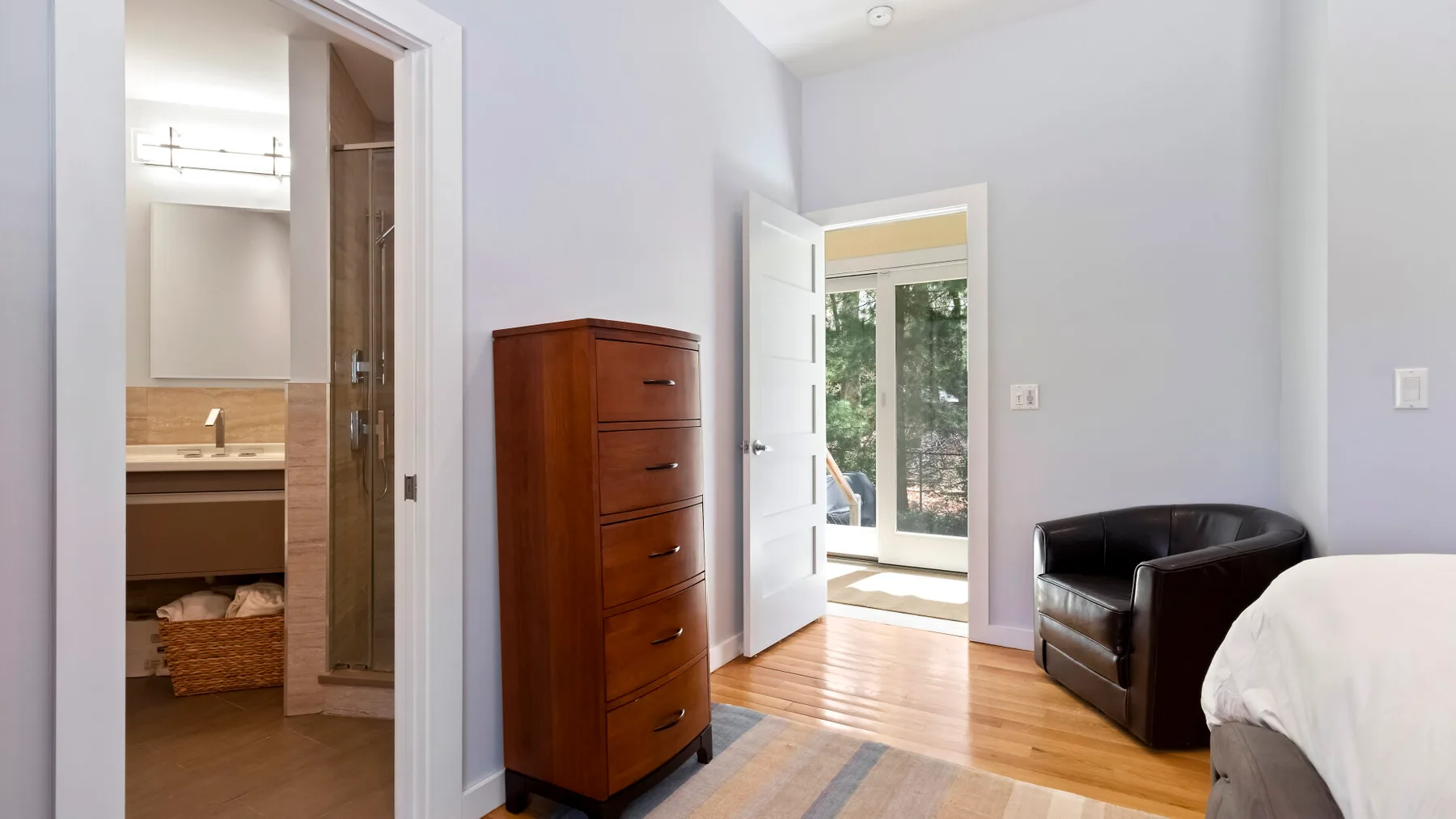 Un dormitorio con un sillón oscuro junto a una cómoda alta de madera.
