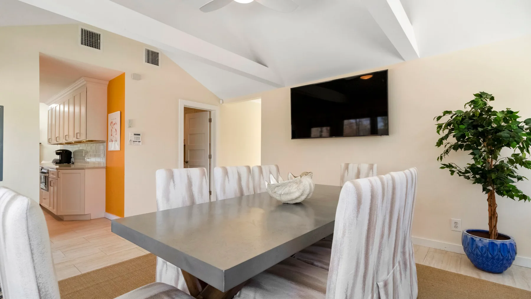 Un comedor con una mesa grande, asientos tapizados y un televisor montado en la pared.