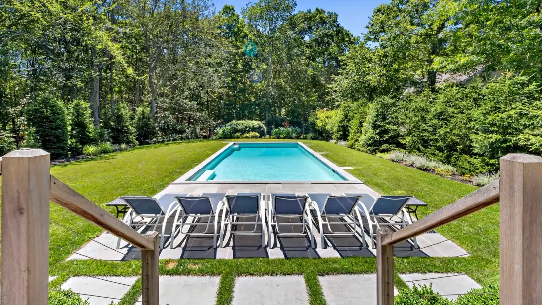 An outdoor pool bordered by lounge seating and a green lawn.