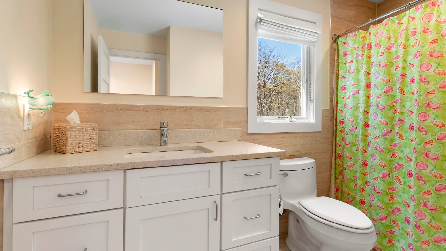 Un baño con un tocador blanco, lavabo y cortina de ducha colorida.
