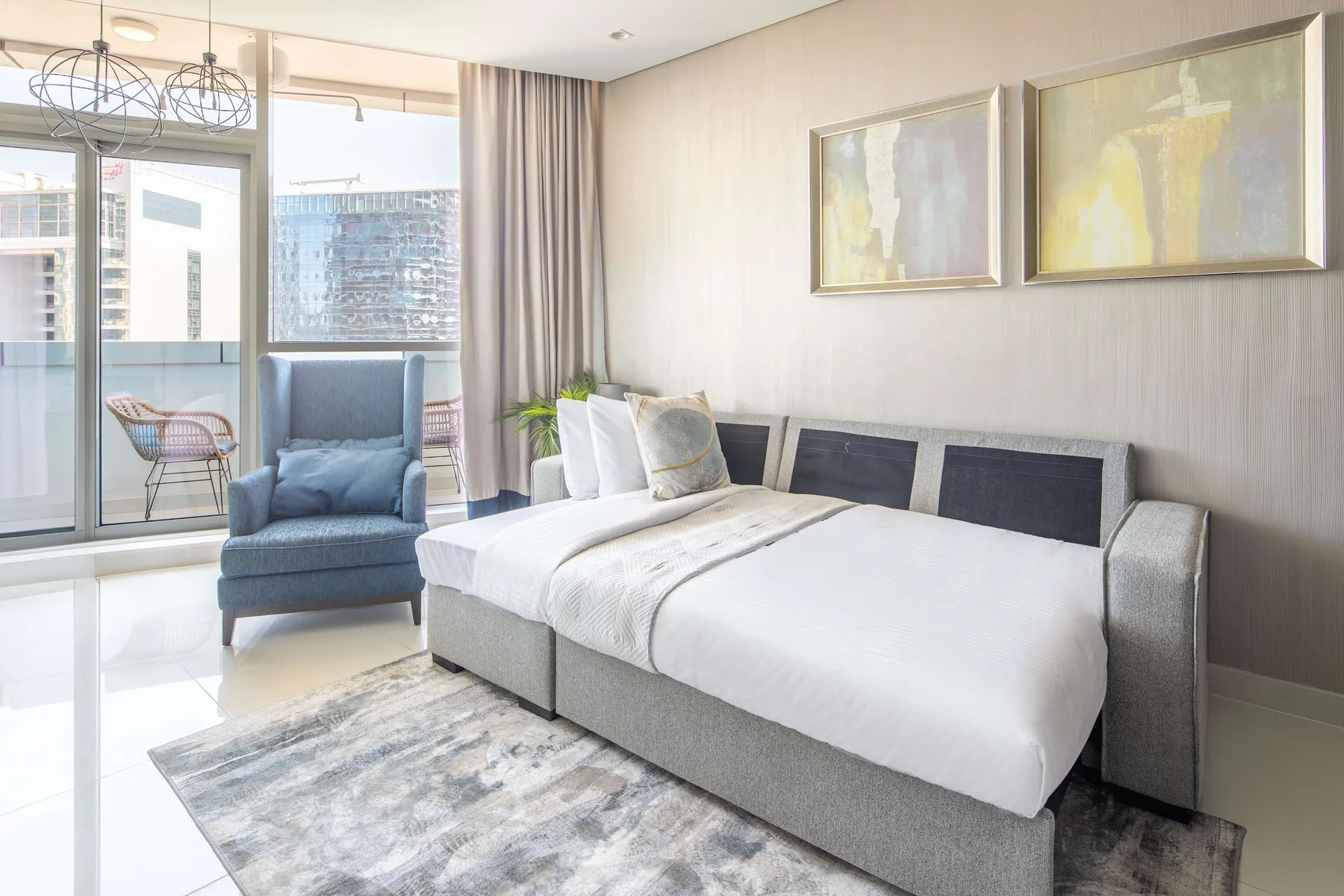 A bright bedroom with a neatly made bed, a blue armchair, and sliding glass doors.