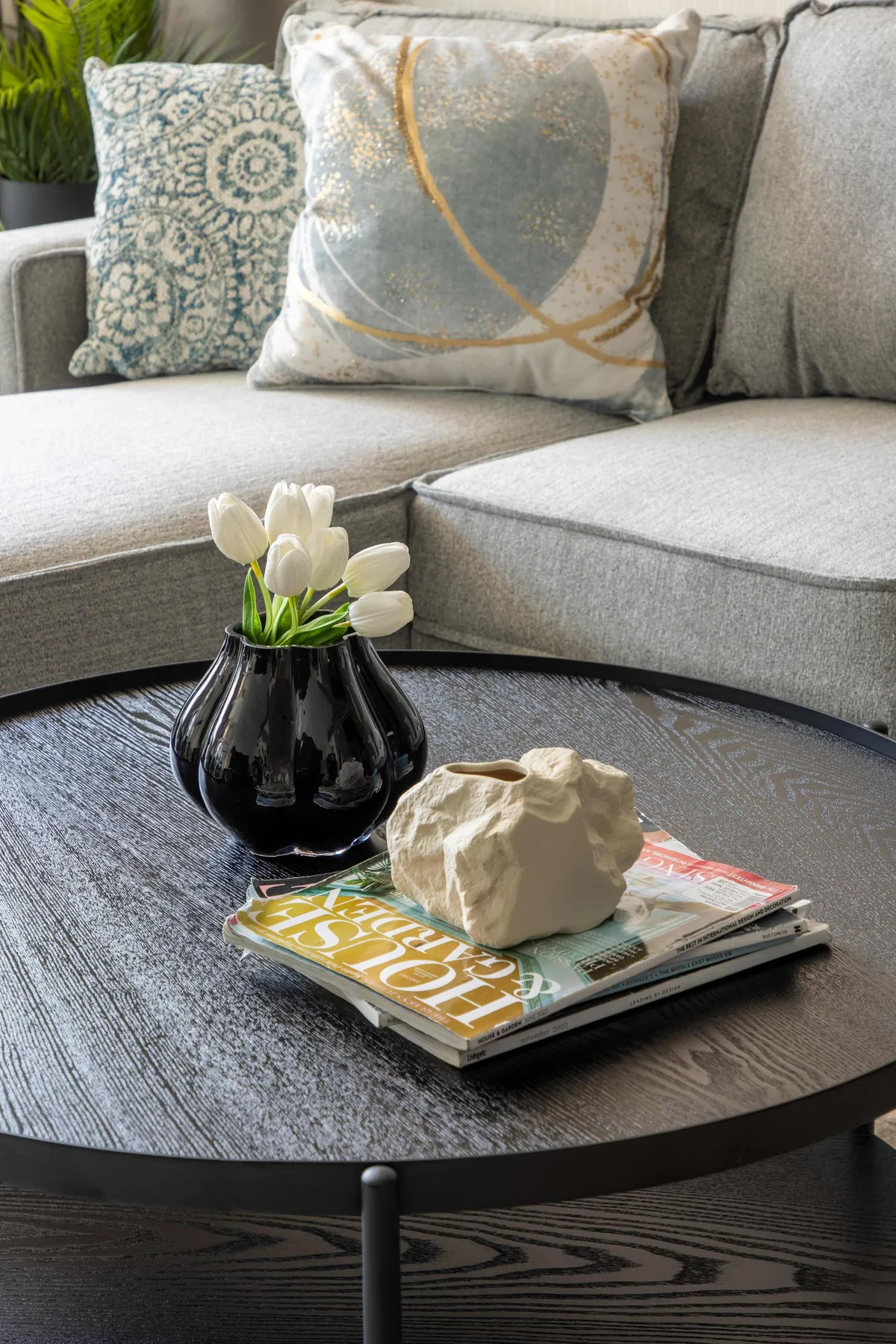 Una zona de estar con cojines decorativos y flores sobre una mesa de centro redonda.