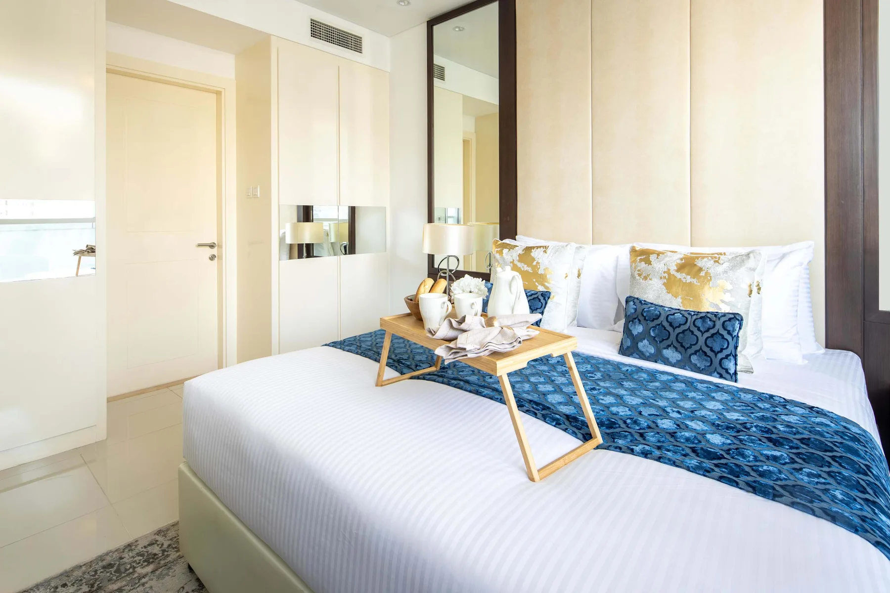 A bright bedroom with white bedding and a blue patterned bed runner.
