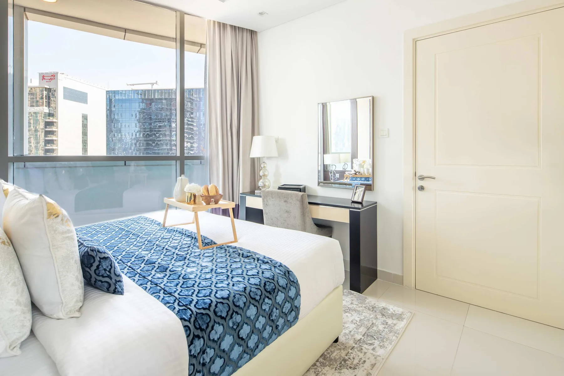A bright bedroom with a bed beside a large window and a writing desk.