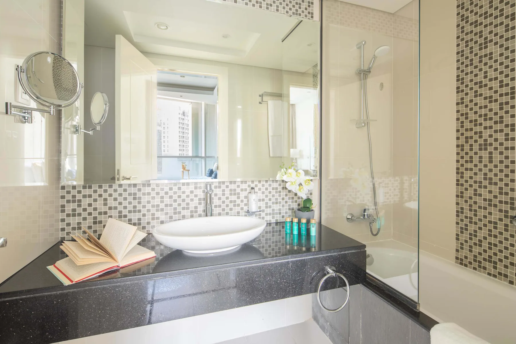 A bright bathroom with a sink vanity, mirror, and glass-enclosed shower.