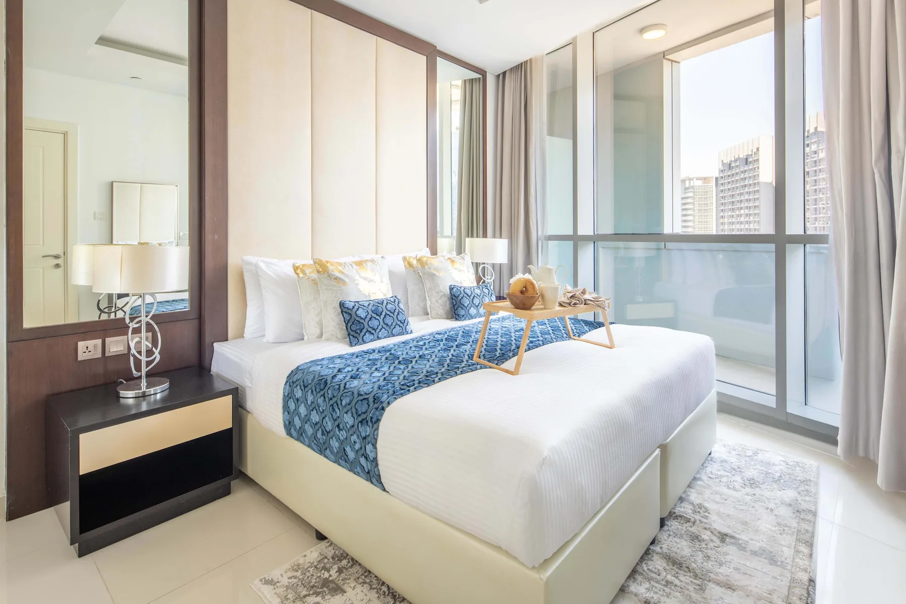 A bright bedroom with a neatly made bed beside floor-to-ceiling windows.