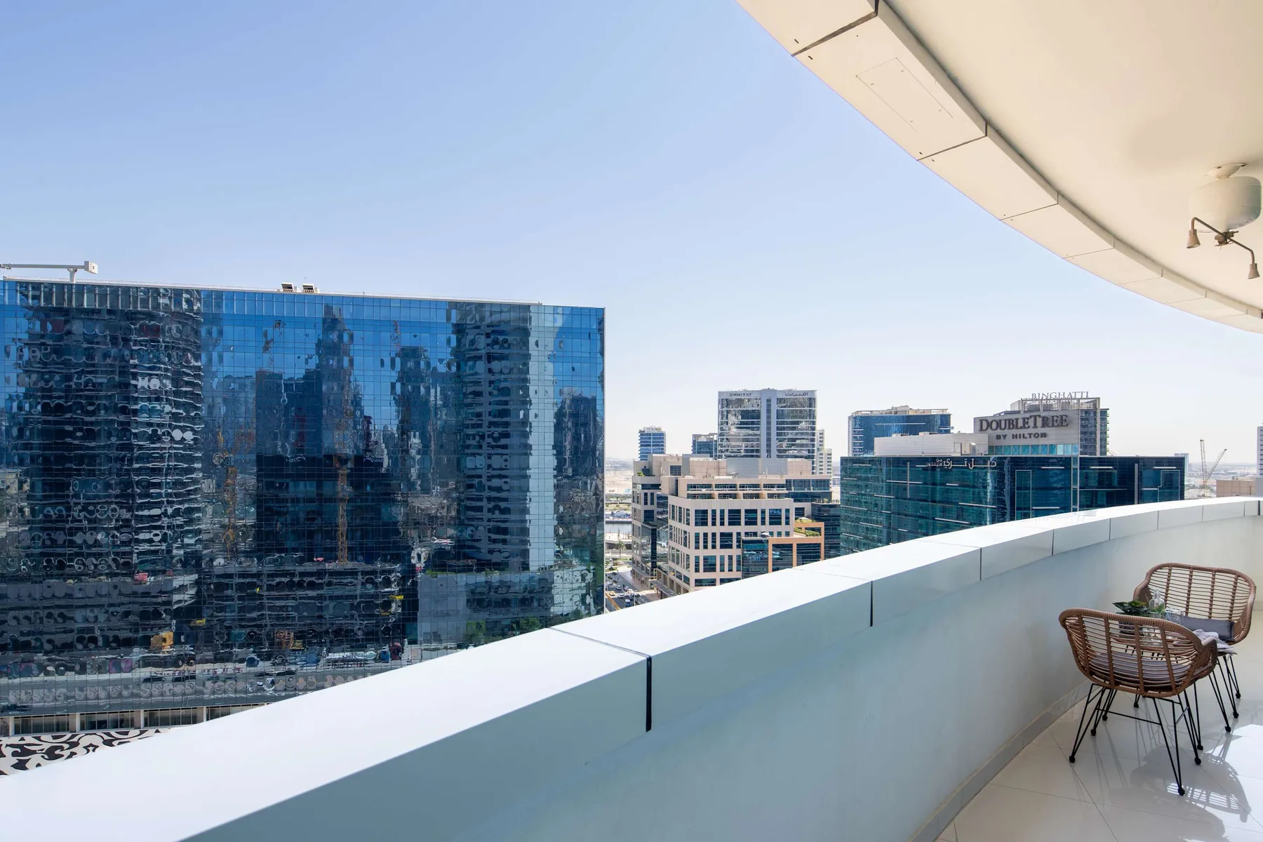 A balcony overlooks nearby office buildings, with a small seating area by the railing.