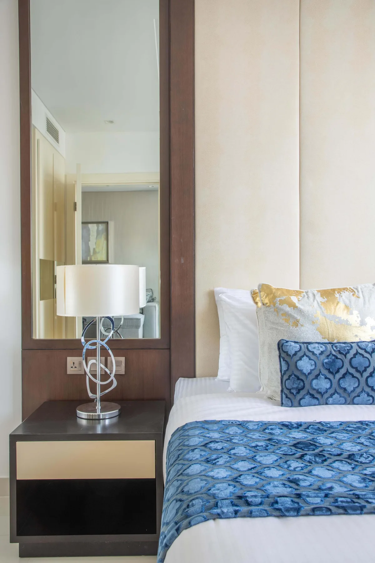 A bedroom with a neatly made bed, blue patterned bedding, and a bedside table.