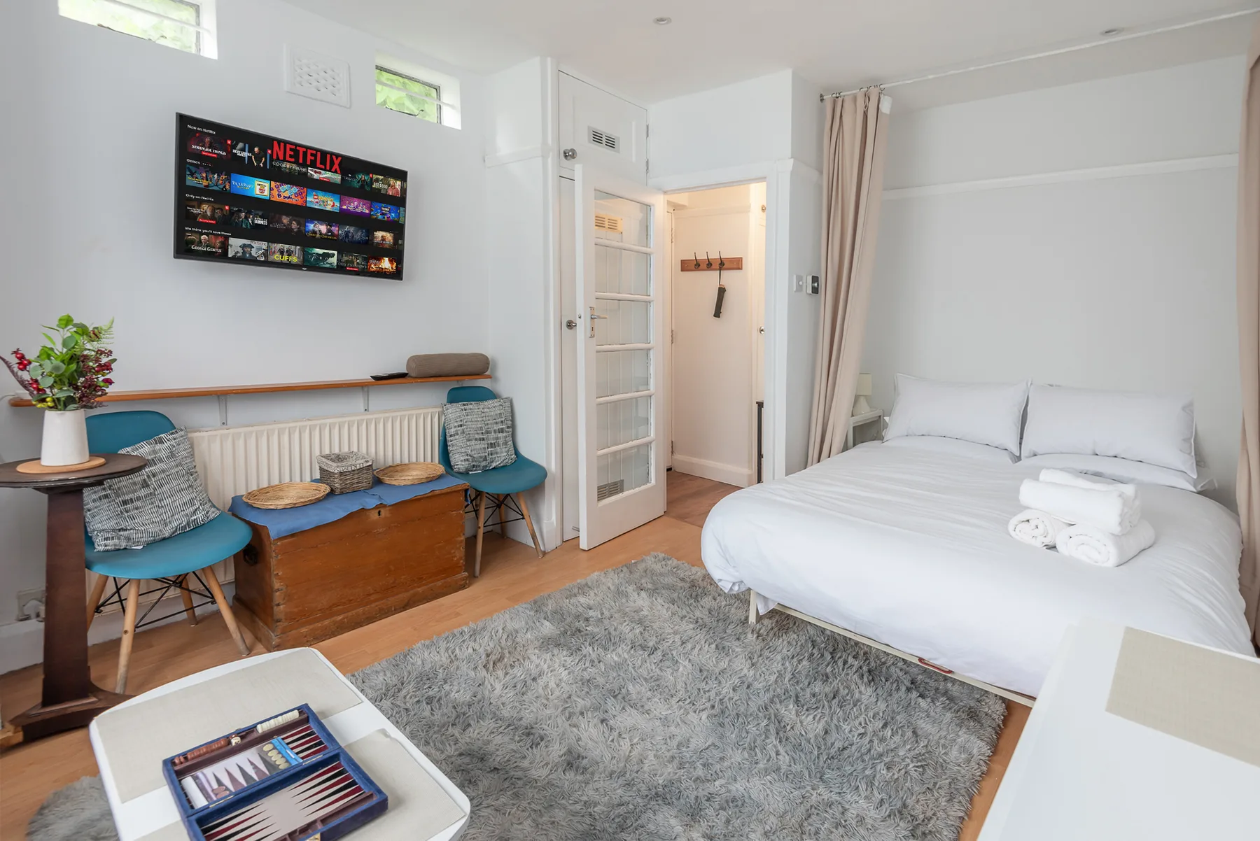 A bright bedroom with a white bed, seating, and a wall-mounted television.