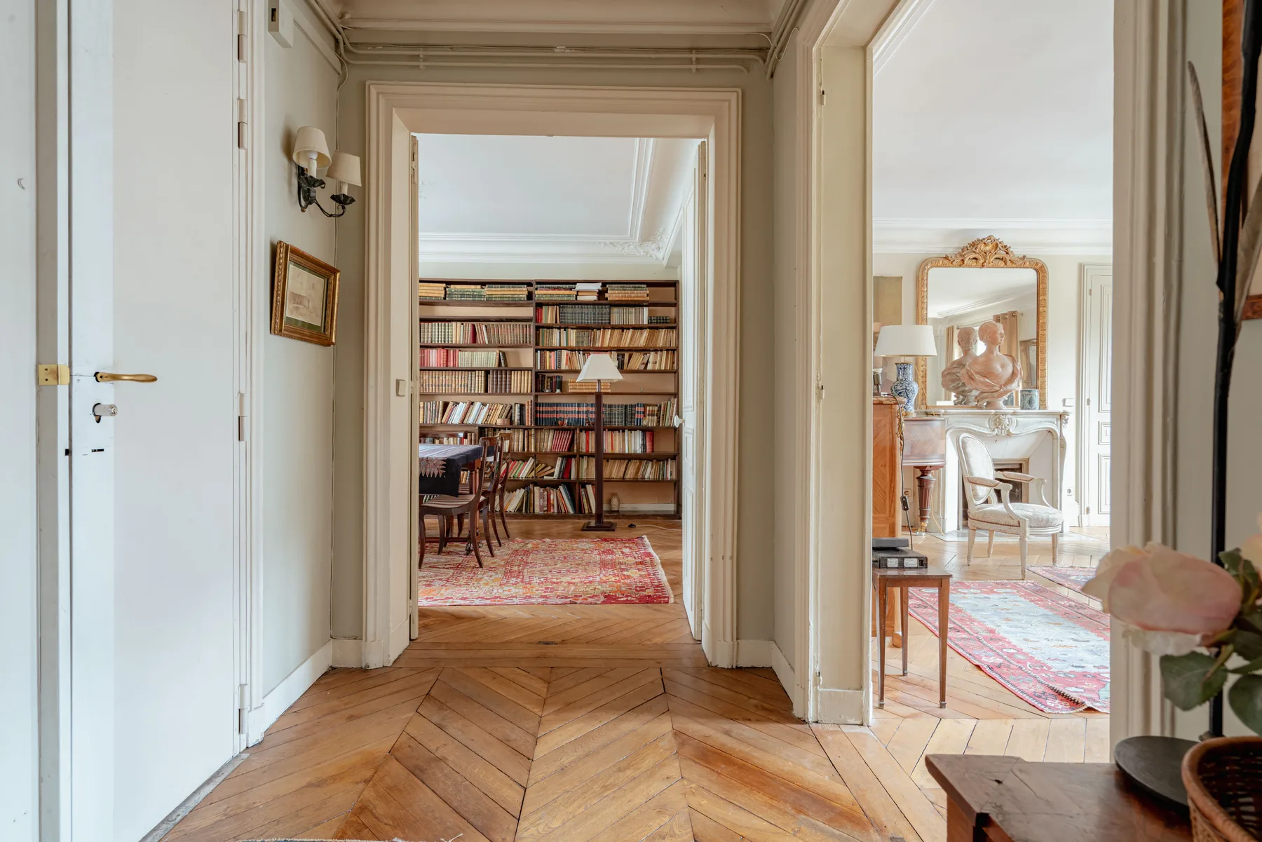 A hallway opens onto a book-lined room and a bright sitting area.