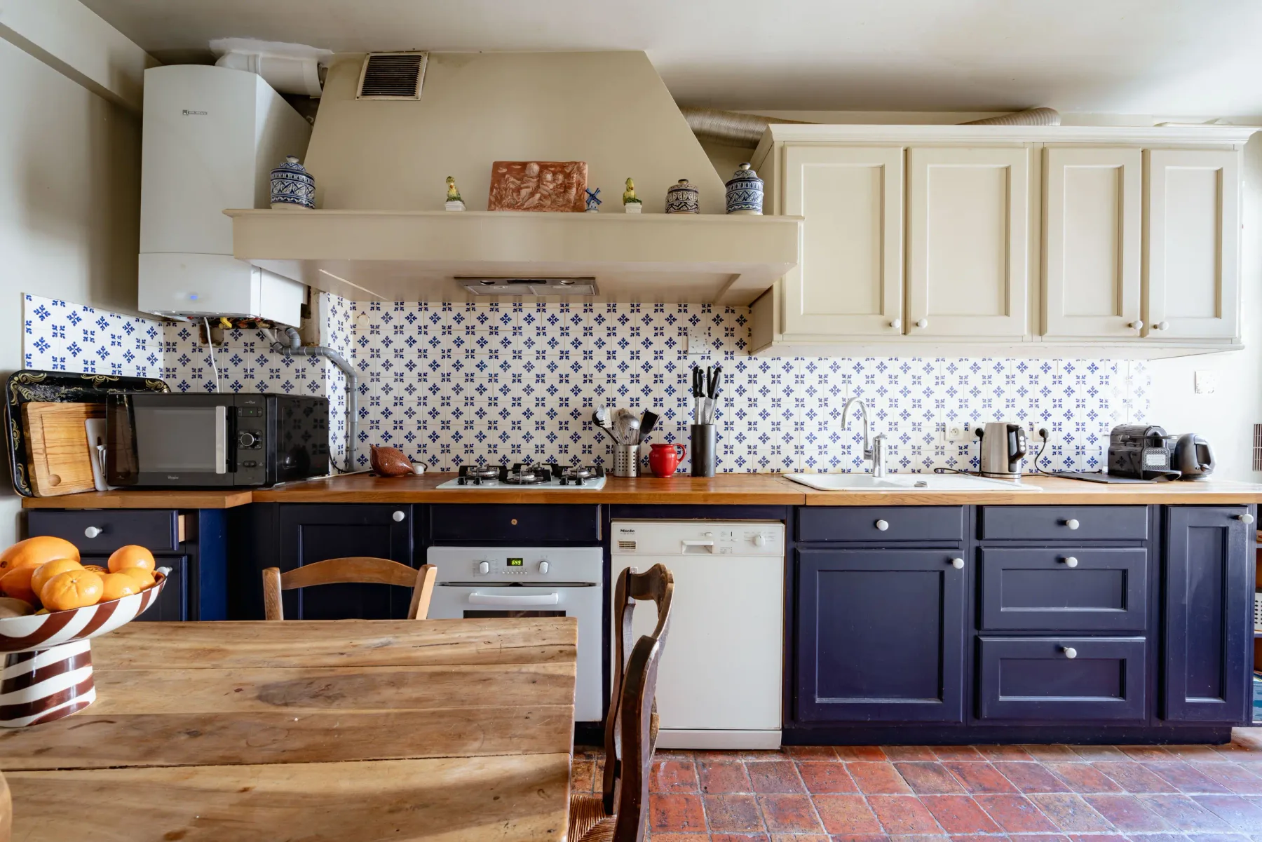 A kitchen with dark lower cabinets, a patterned backsplash, and a wooden table.