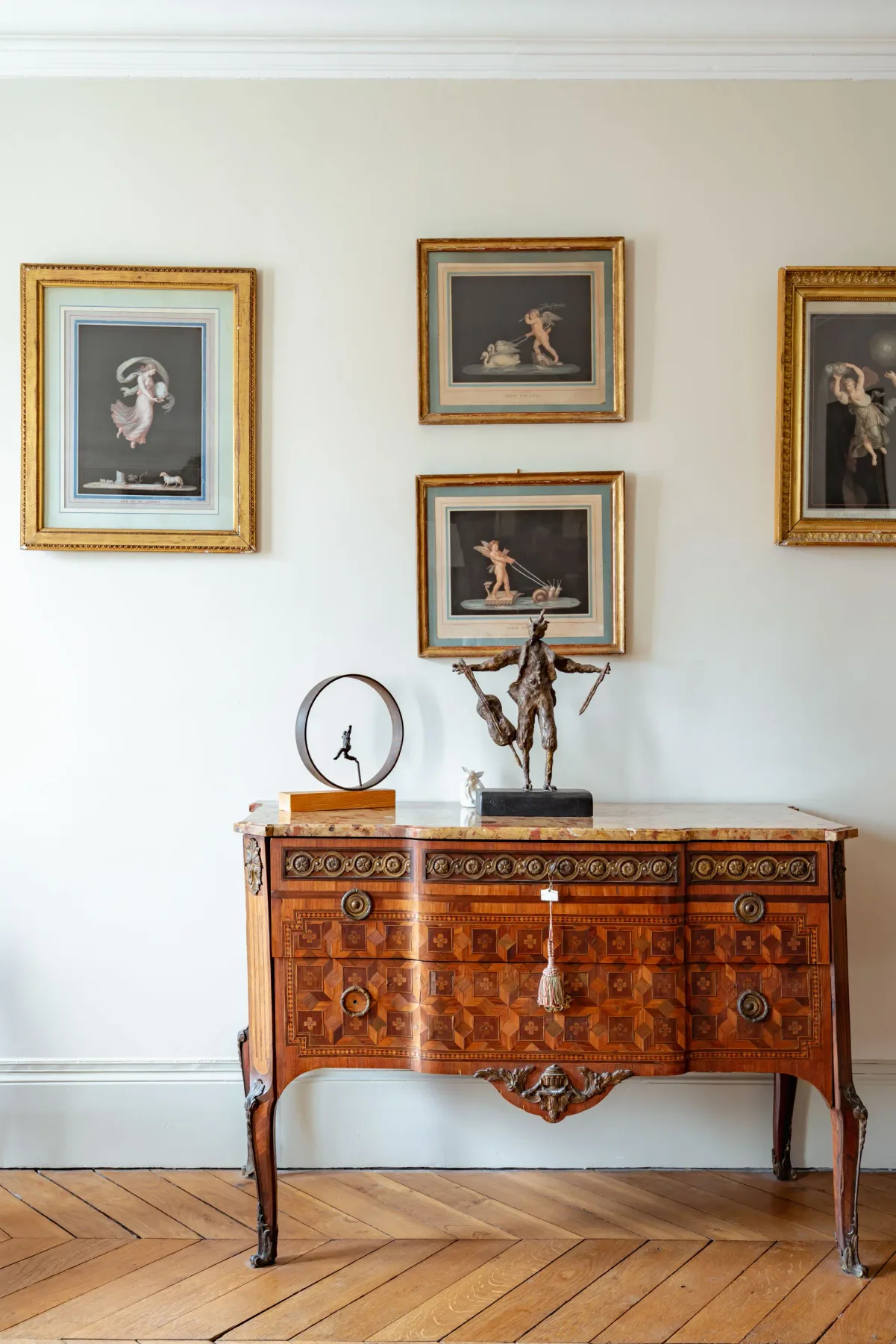 A wooden cabinet stands beneath framed artwork against a white wall.