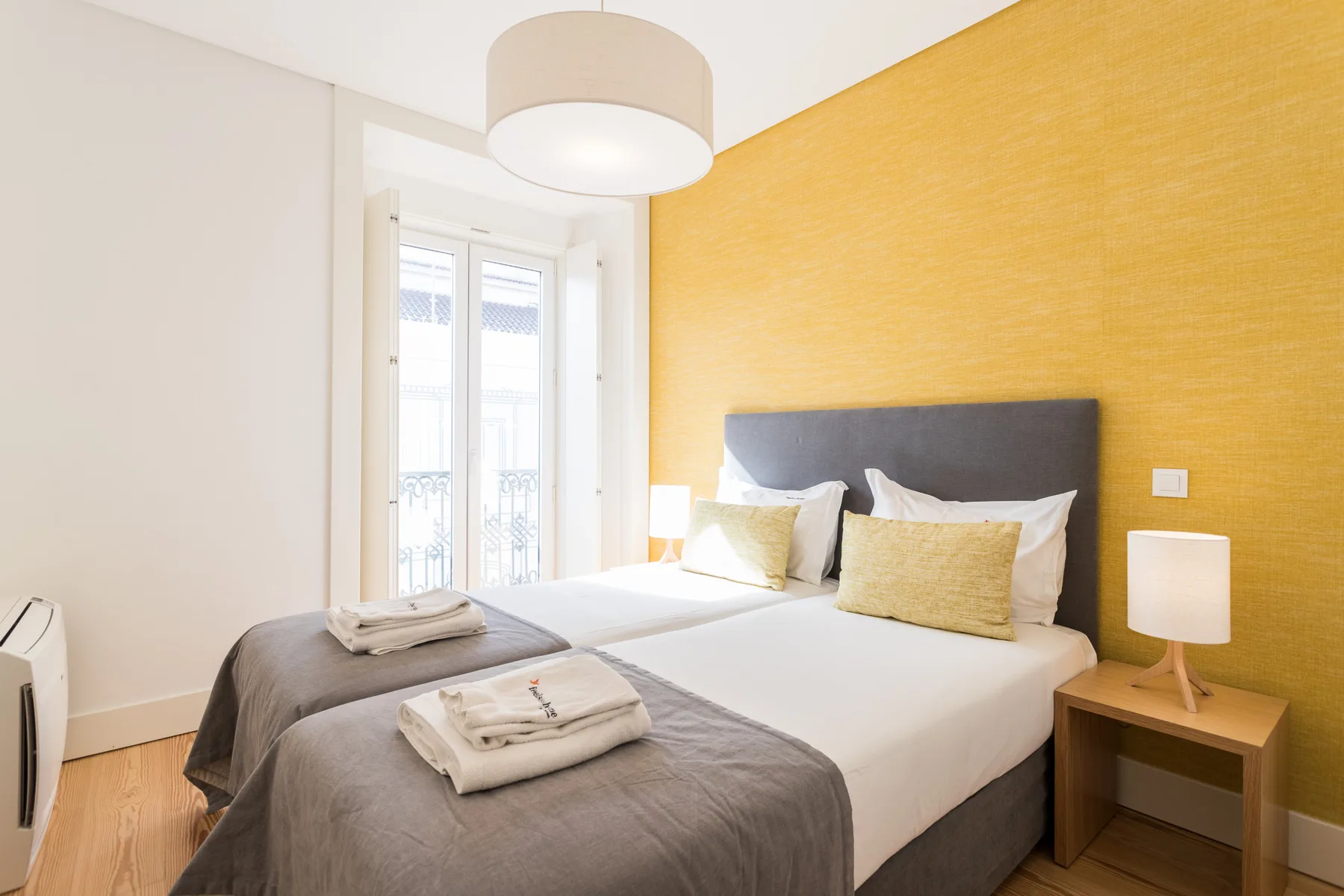 A bedroom with a bed, folded towels, and a bright window.