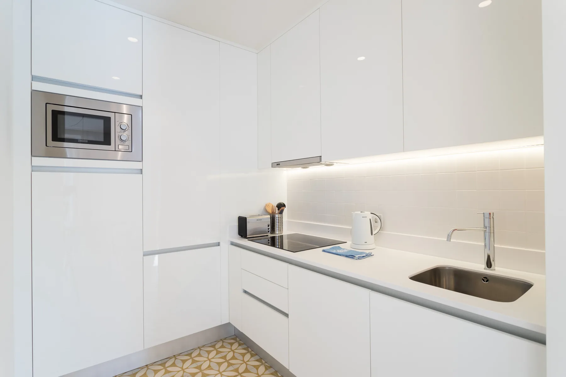 A bright modern kitchen with white cabinetry, a cooktop, and a sink.