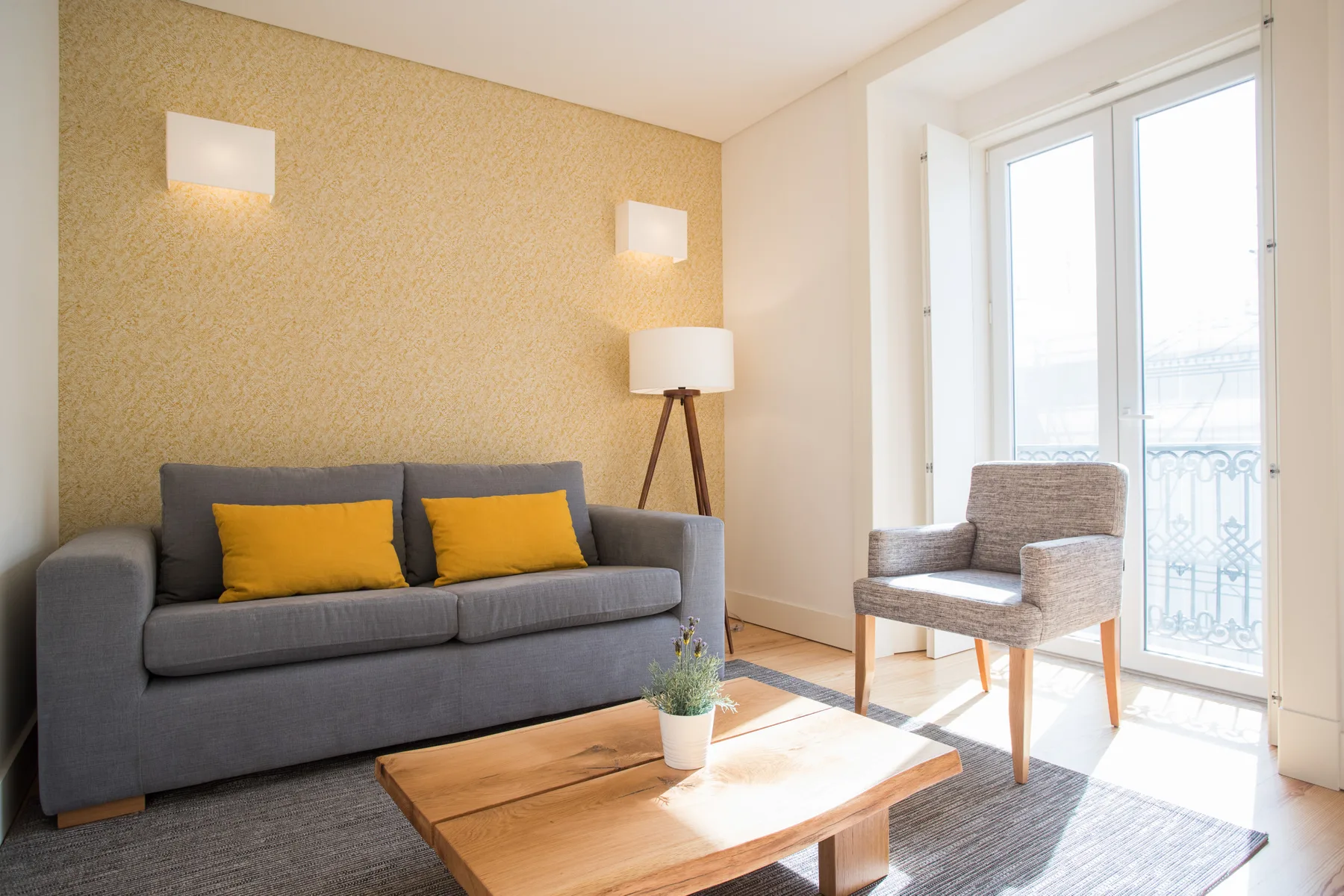 A living room with a gray sofa, wooden coffee table, and bright balcony doors.