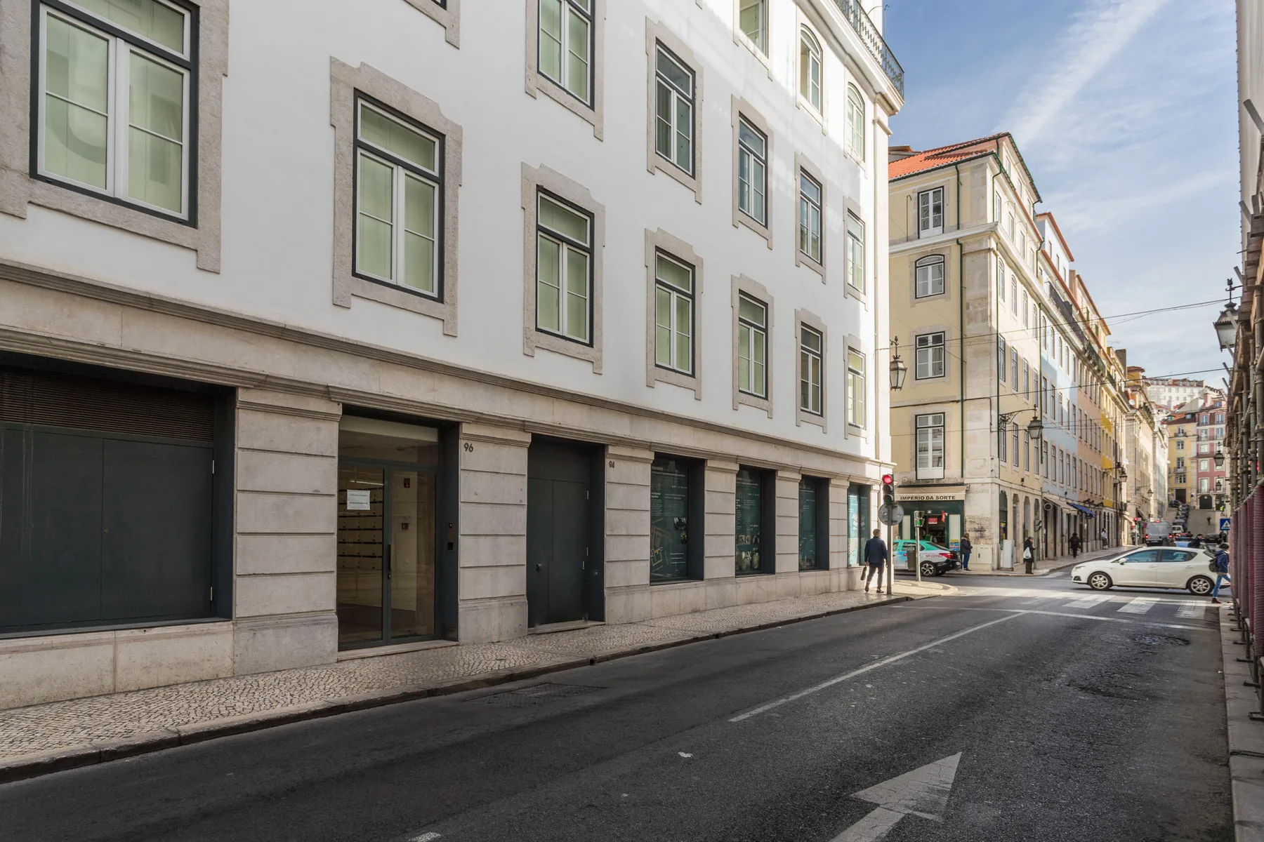 A narrow city street lined with multistory buildings and parked cars.