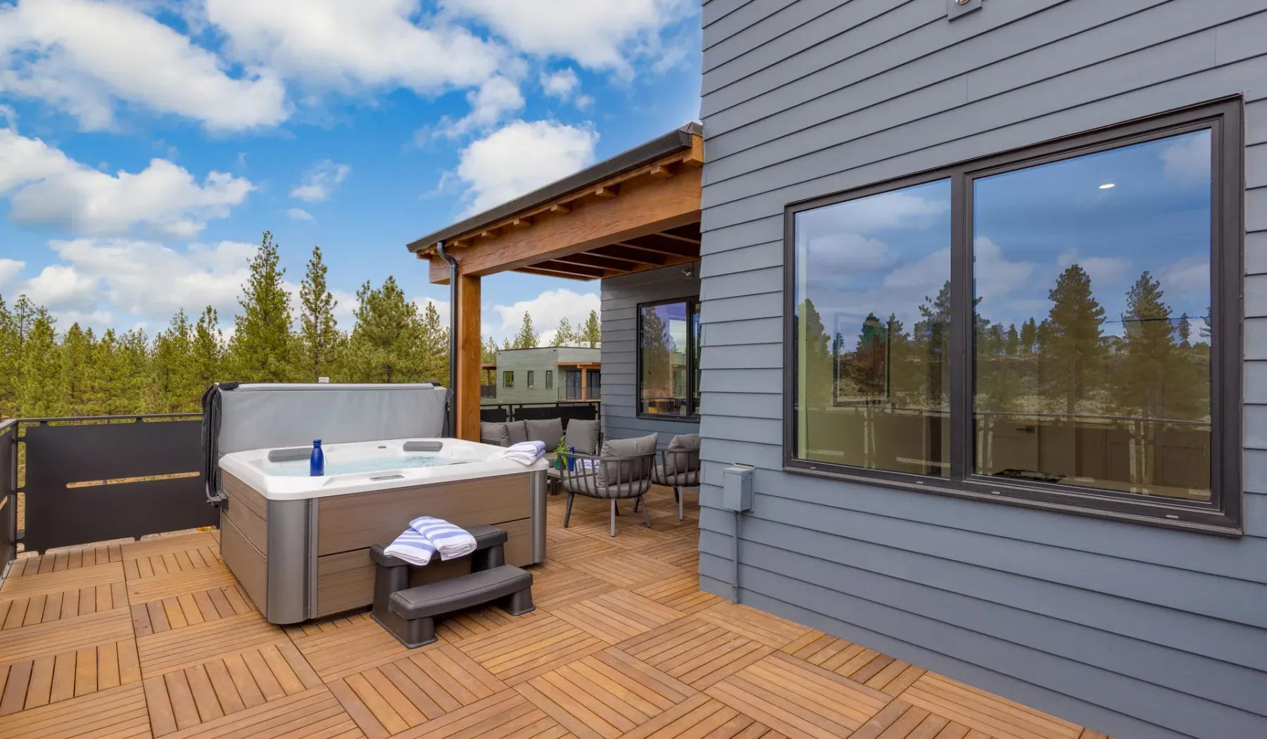 An outdoor deck with a hot tub and seating beside a modern building.