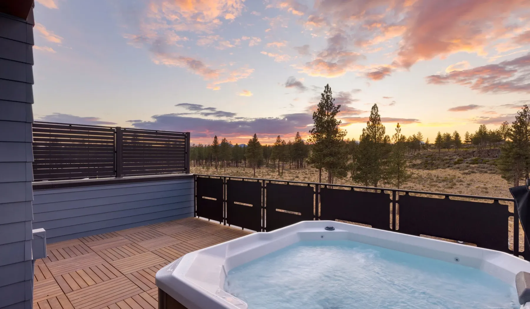 An outdoor hot tub sits on a wooden deck overlooking trees beneath a colorful sunset sky.