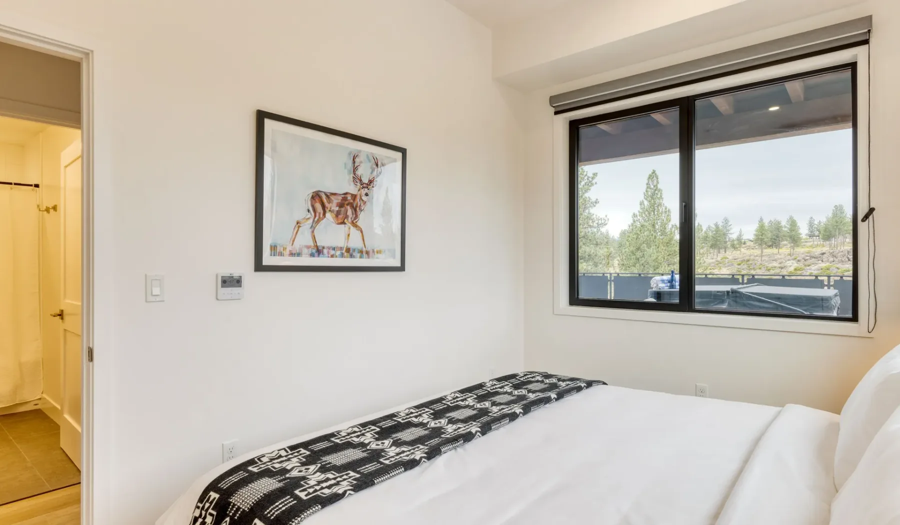 A bedroom with a bed beside a large window overlooking trees.