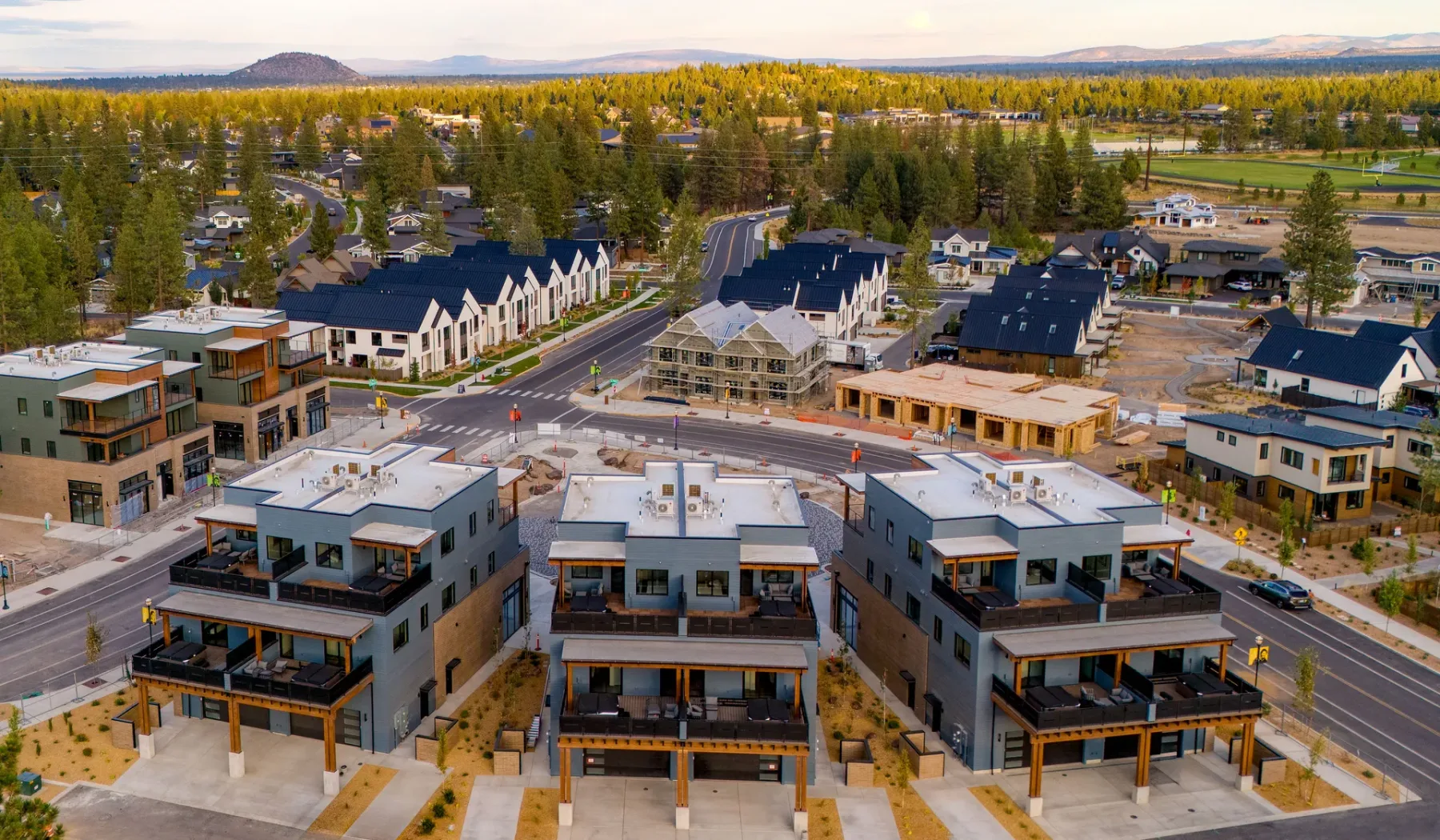 An aerial view of a residential neighborhood with modern buildings and tree-covered hills beyond.