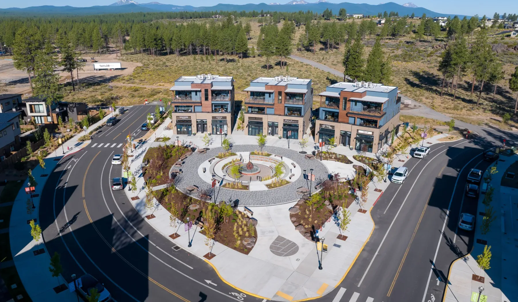 An aerial view of modern buildings around a landscaped plaza and circular fountain.