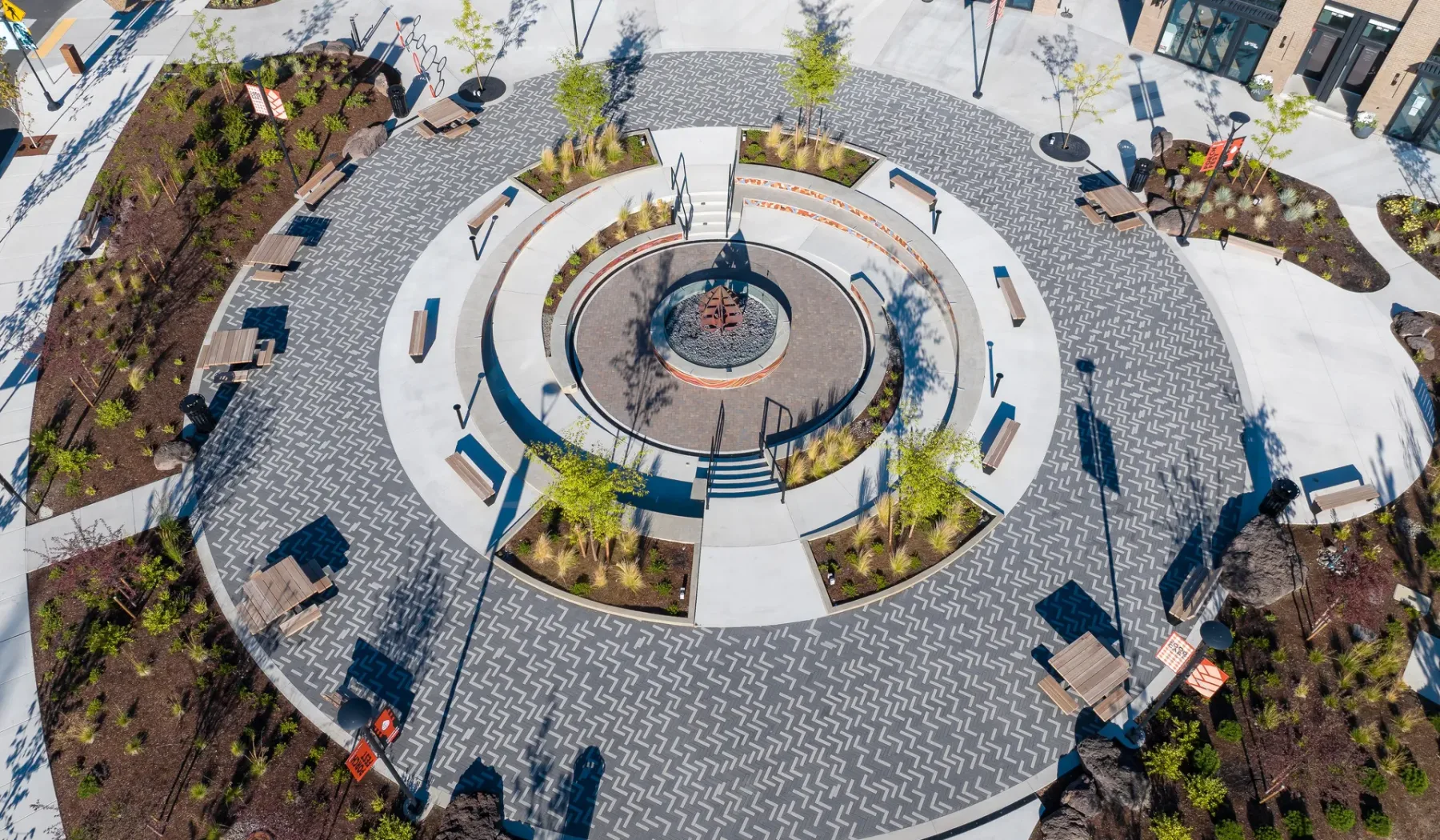 A circular paved plaza surrounds a central fountain, with benches and planted areas.