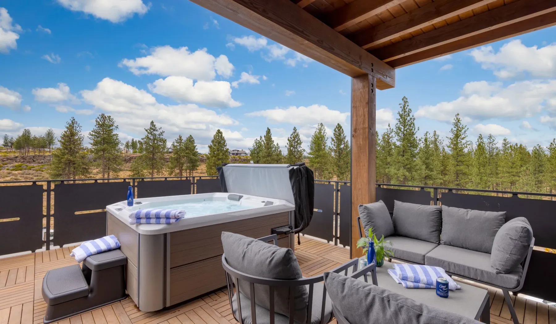 A hot tub and outdoor seating sit beneath a wooden pergola on a deck.