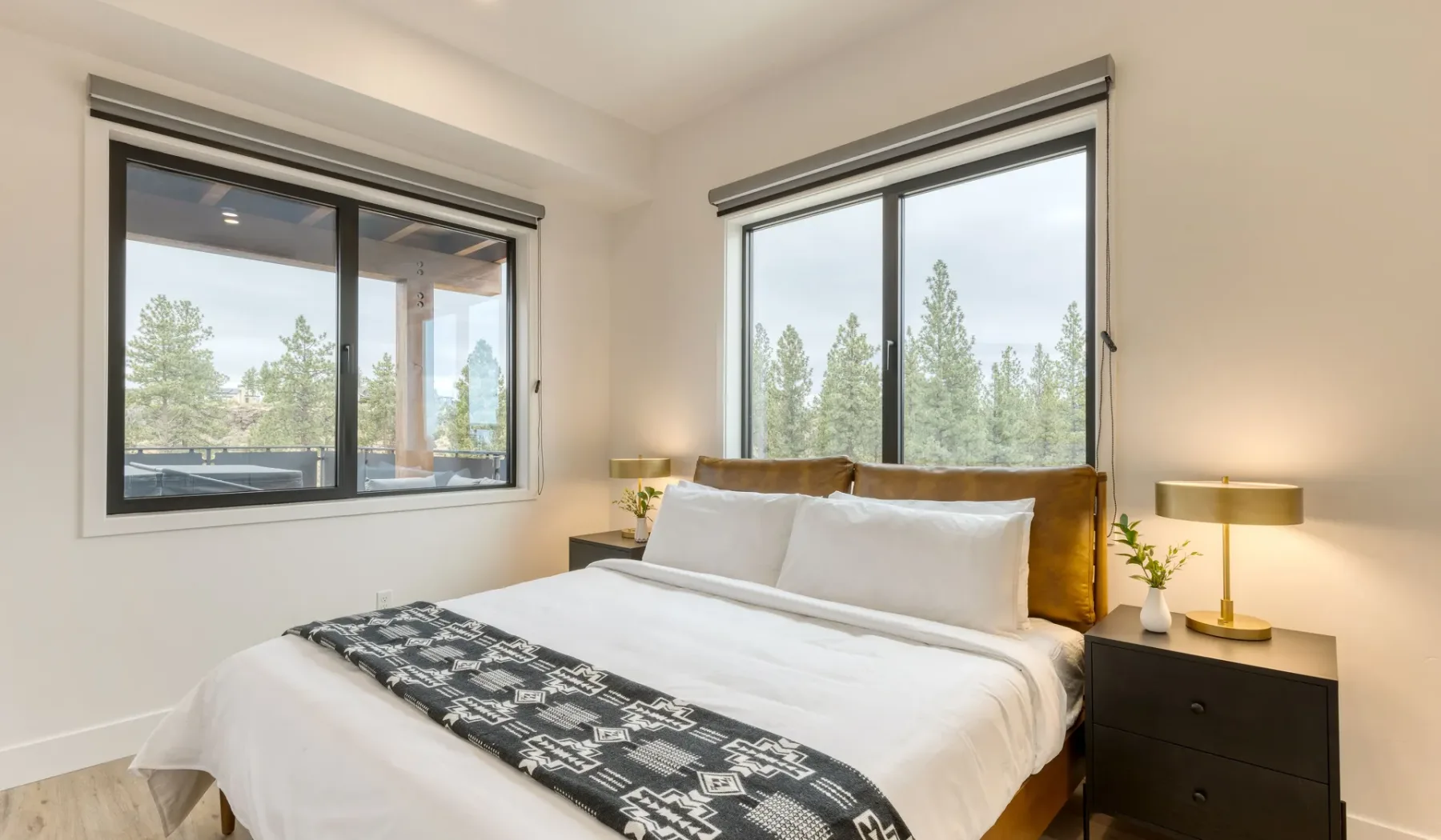 A bright bedroom with a neatly made bed between two large windows.