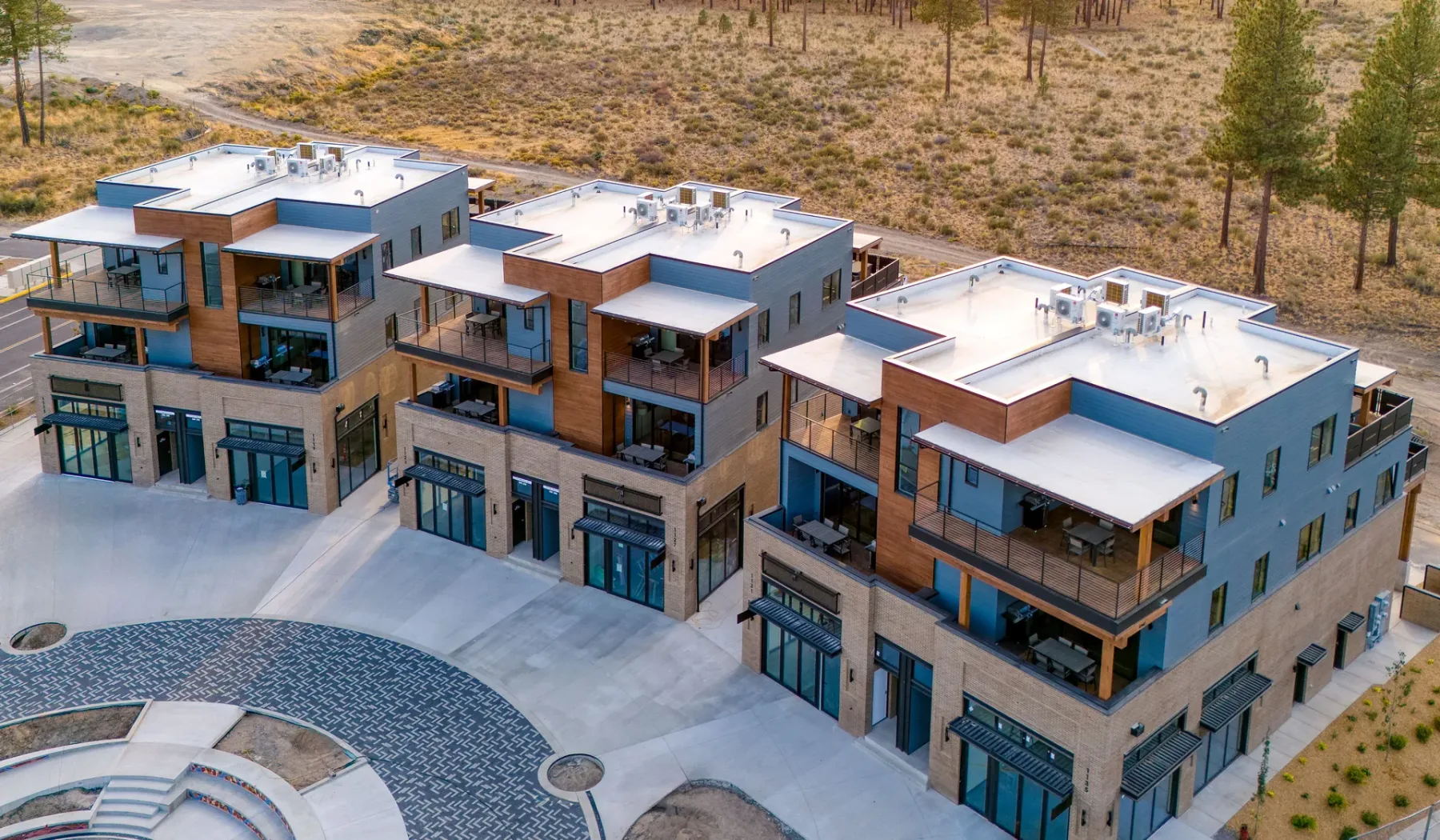 A modern multi-unit building overlooks a paved courtyard in a dry, wooded landscape.
