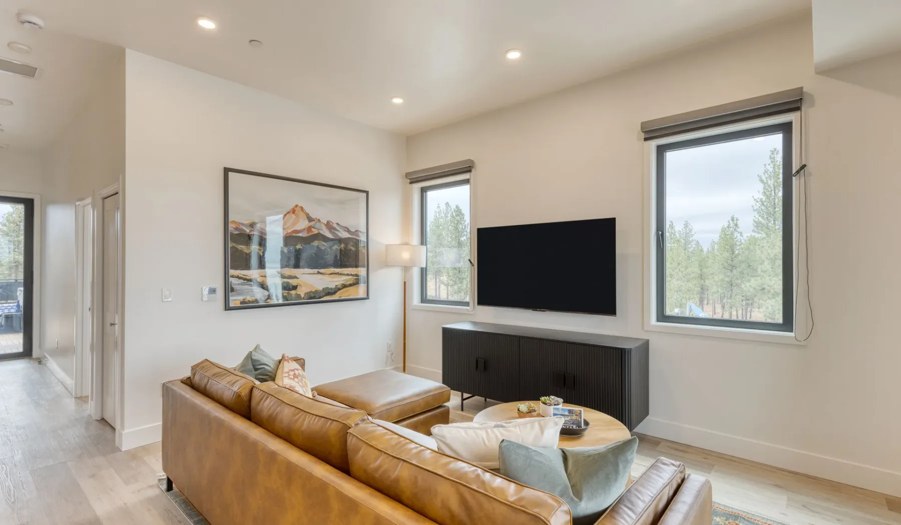 Una sala luminosa con asientos de cuero, un televisor y grandes ventanas.