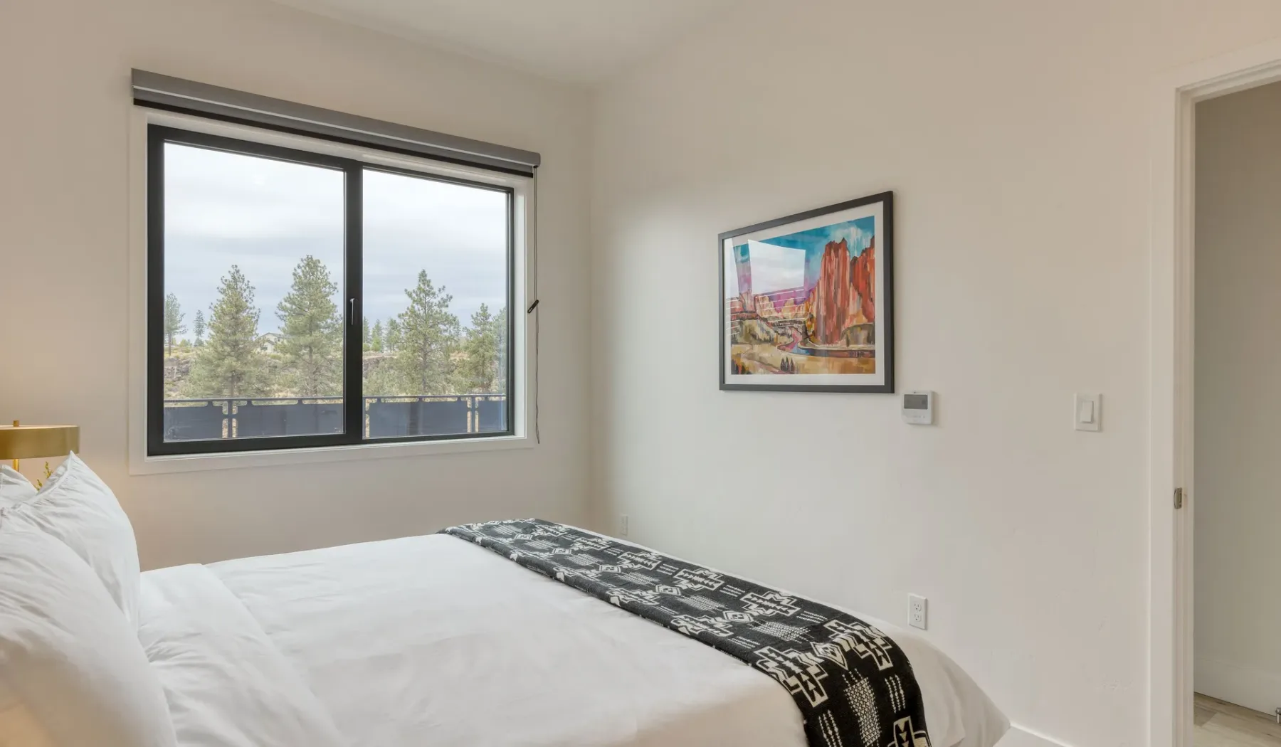 A bright bedroom with a bed beside a large window overlooking trees.
