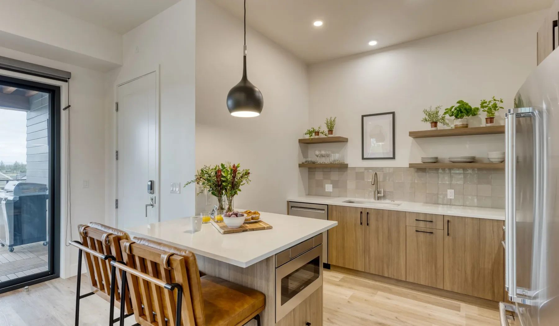 A bright kitchen with a large island, wooden seating, and open shelves.