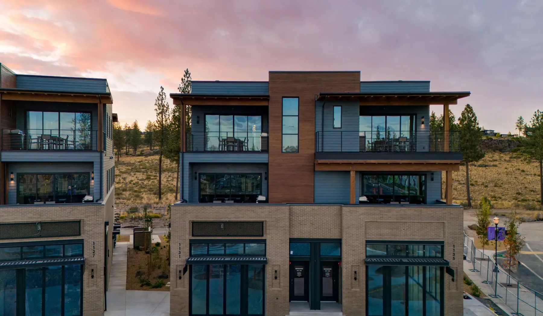 Edificios modernos de varias plantas con grandes ventanas bajo un cielo colorido al atardecer.
