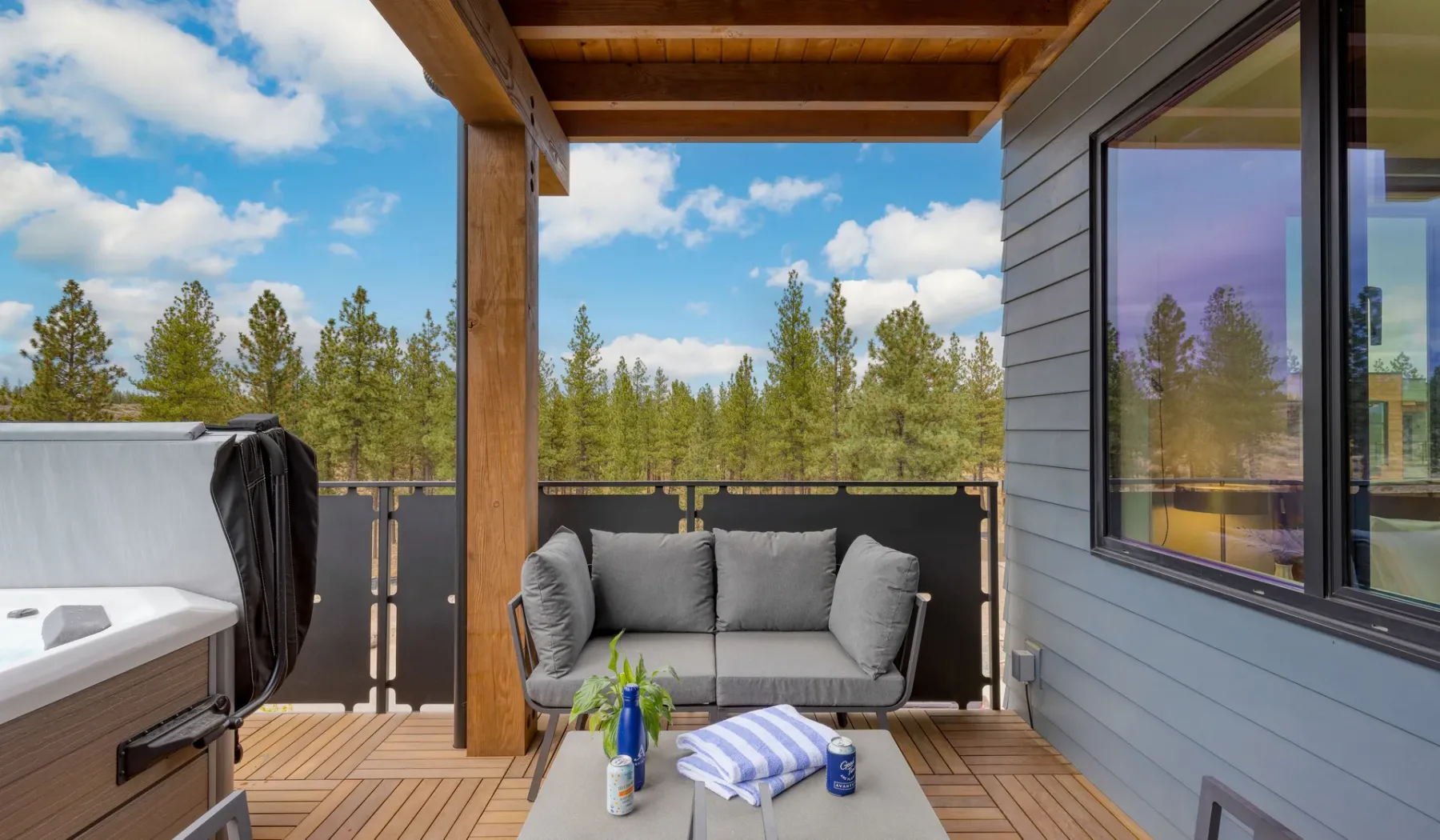 A covered outdoor deck has a gray seating area overlooking trees.