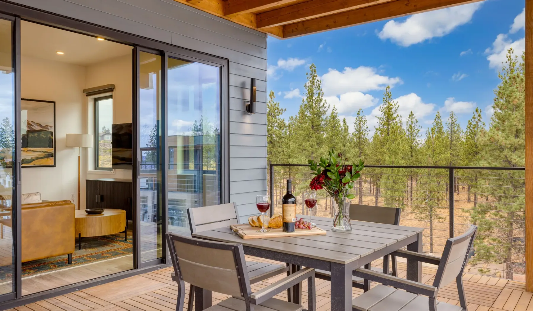An outdoor dining area on a deck overlooks trees beneath a clear blue sky.