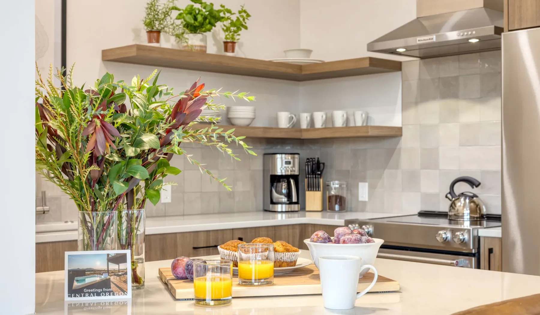 A bright kitchen counter displays a vase of greenery, breakfast items, and a coffee maker.
