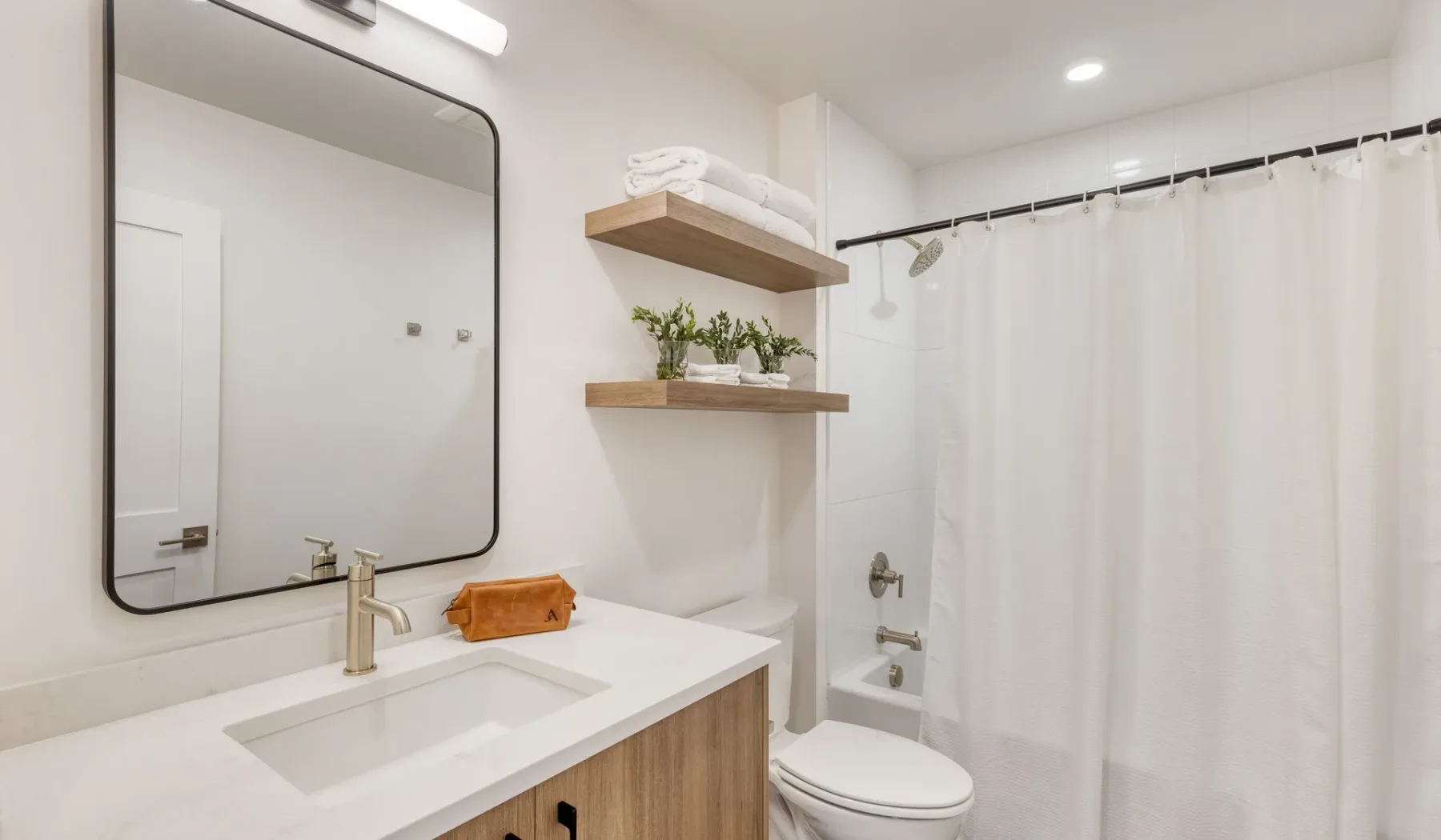 A bright bathroom with a sink, mirror, toilet, and shower curtain.