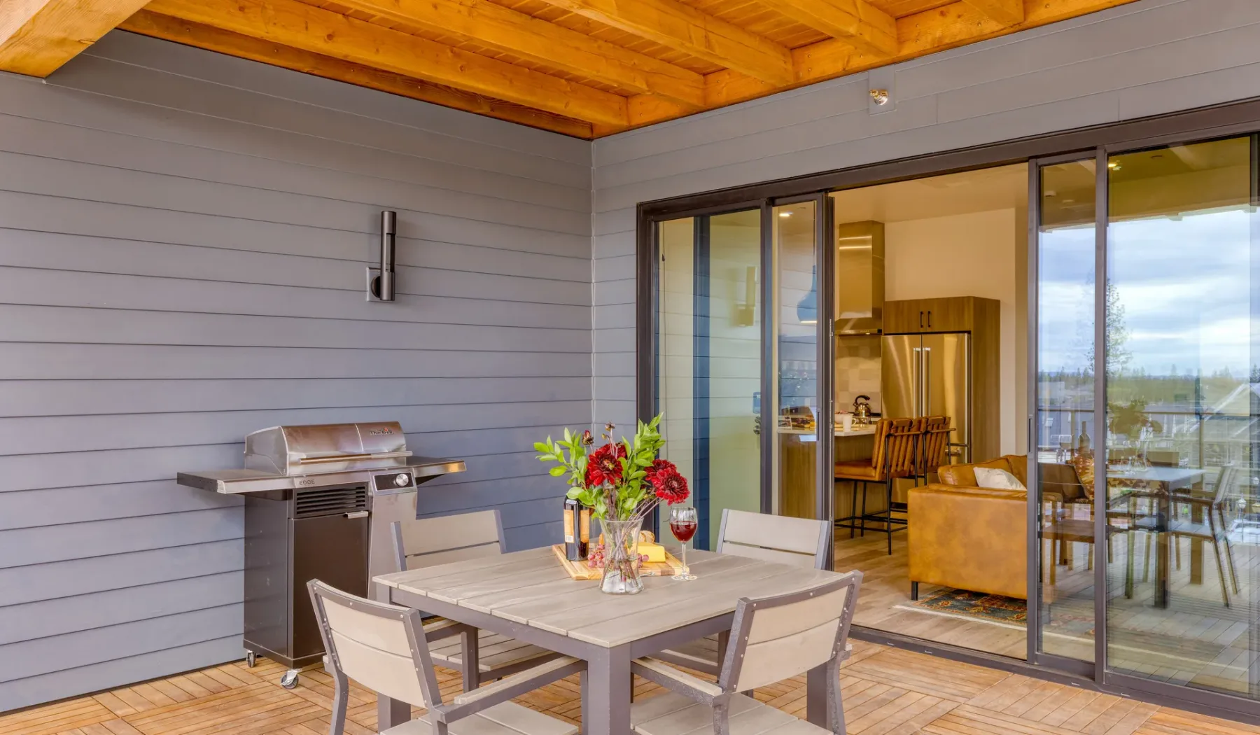 A covered patio has a dining table and grill beside sliding glass doors.