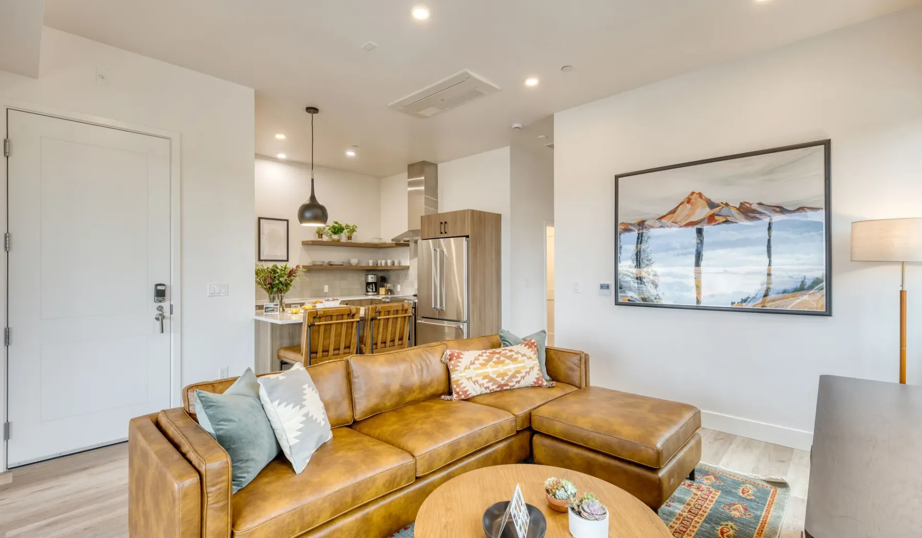 A bright open-plan living room with leather seating and a kitchen beyond.
