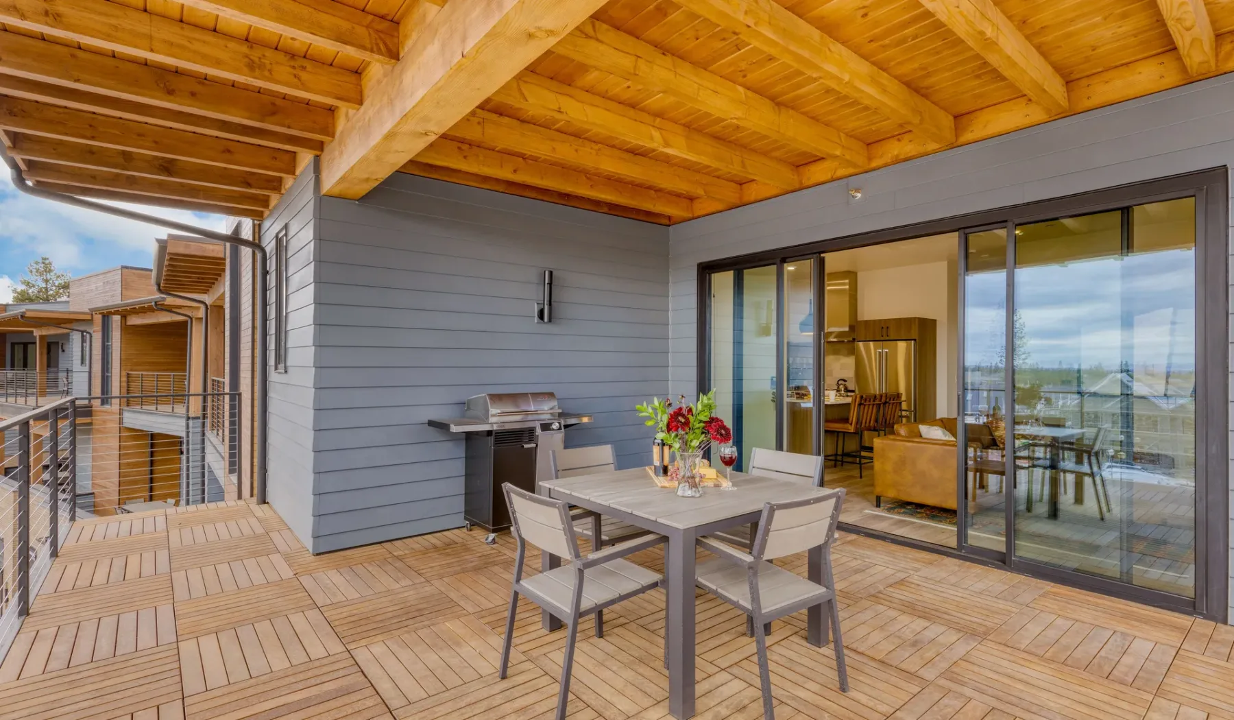 A covered wooden deck has an outdoor dining table beside sliding glass doors.
