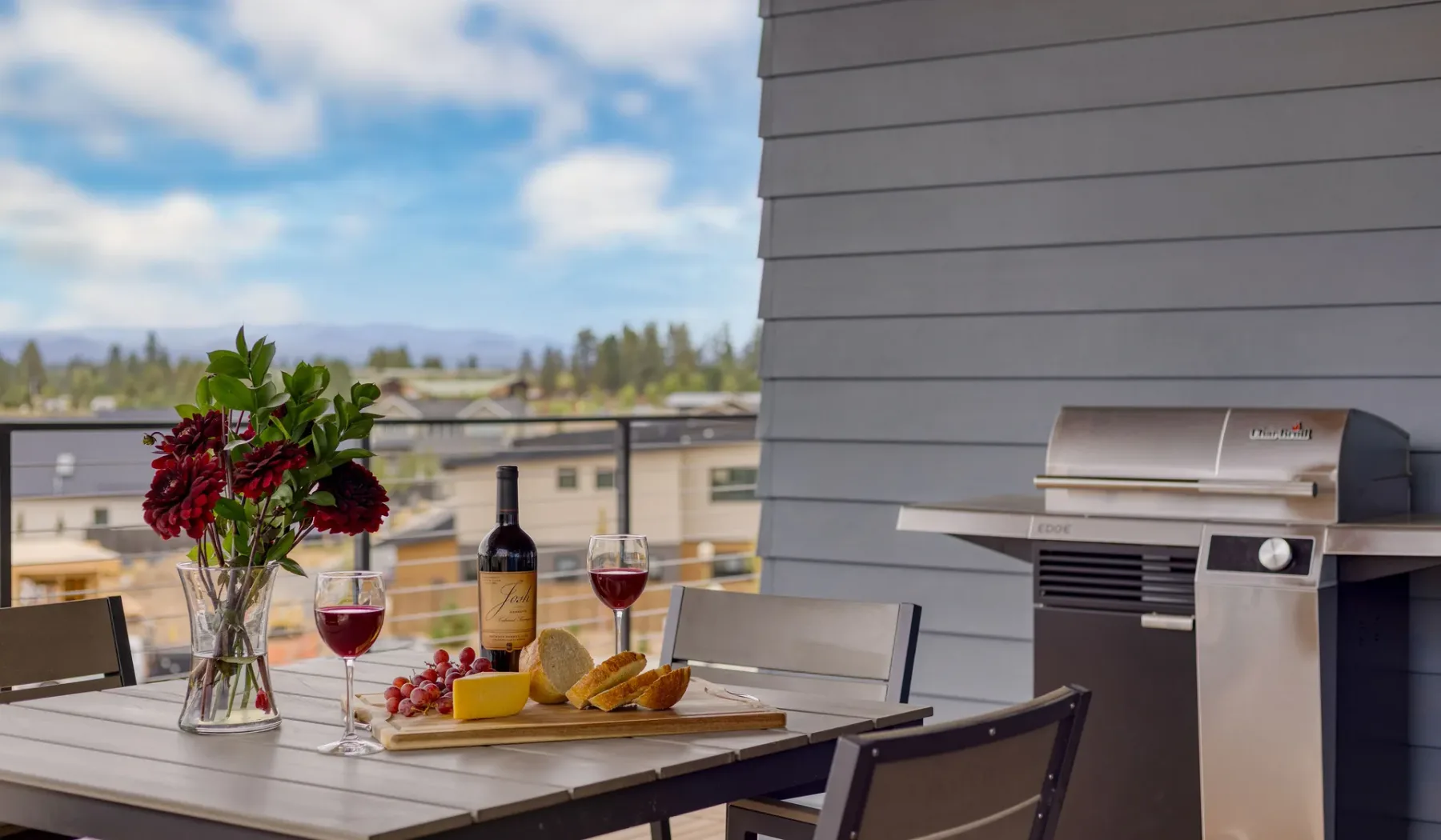 A balcony dining area with a table, flowers, and an outdoor grill.