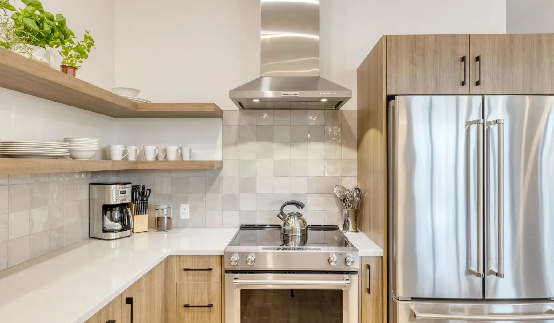 A bright kitchen with a stove, range hood, and stainless steel refrigerator.