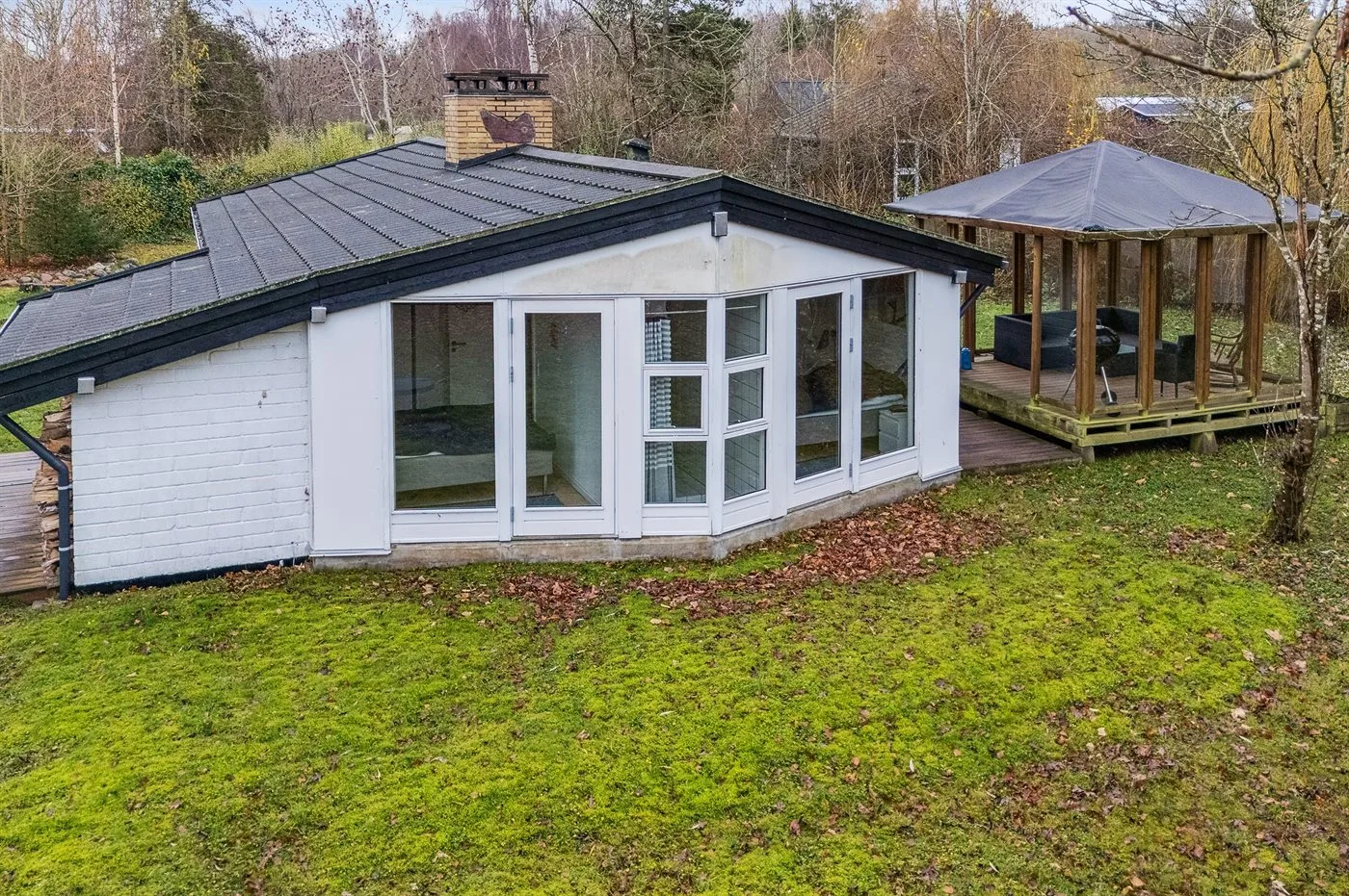 A white house with a dark sloped roof and a covered wooden deck.
